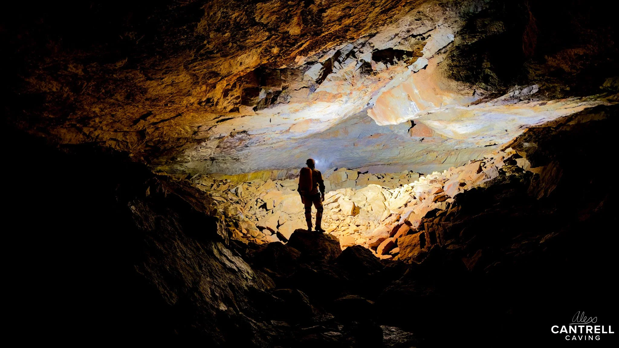 Silhouette of a person standing in a brightly lit cave with rocky walls and ceiling.