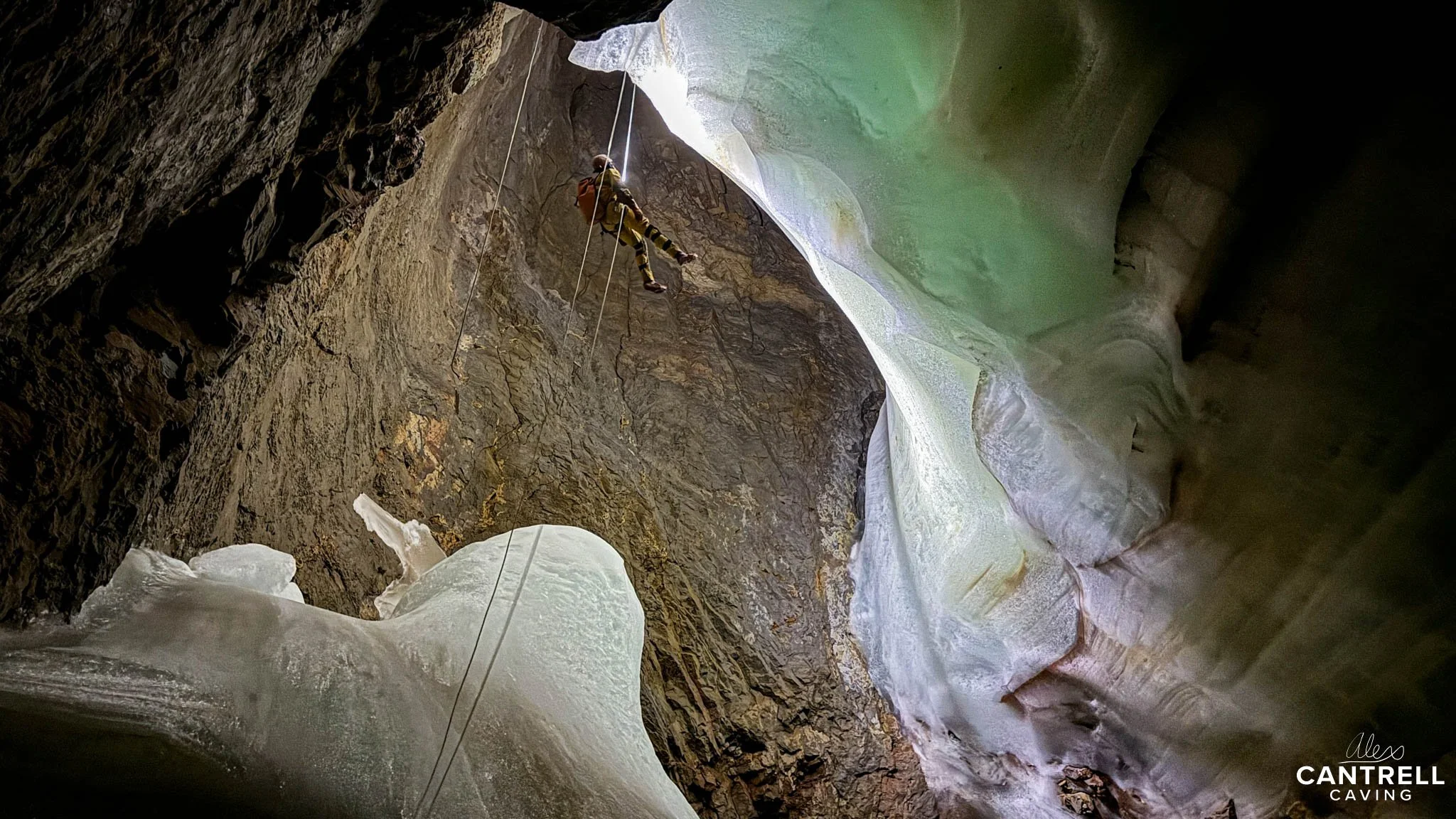 Person rappelling down a rocky cave with icy formations.