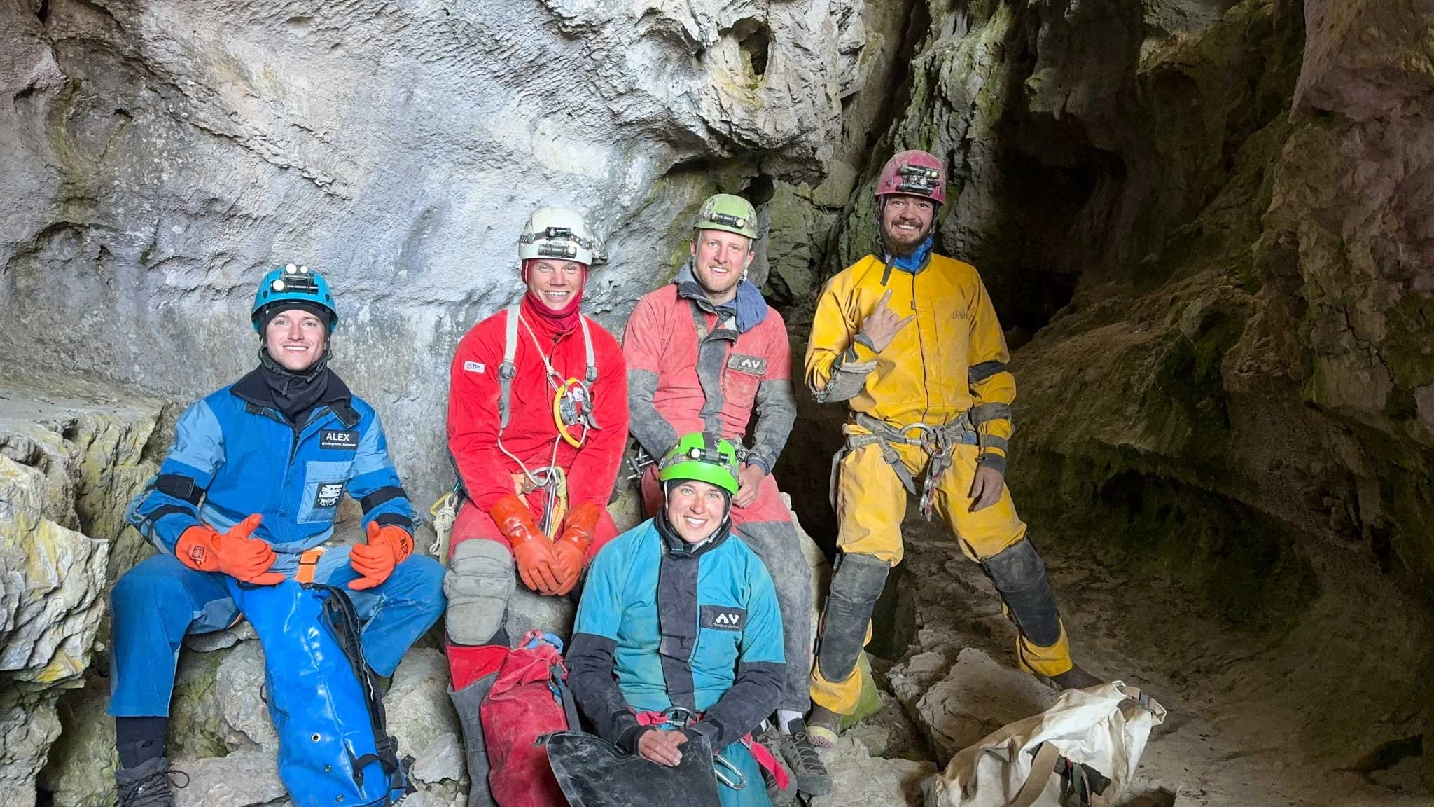Group of cavers wearing helmet lamps and suits inside a cave