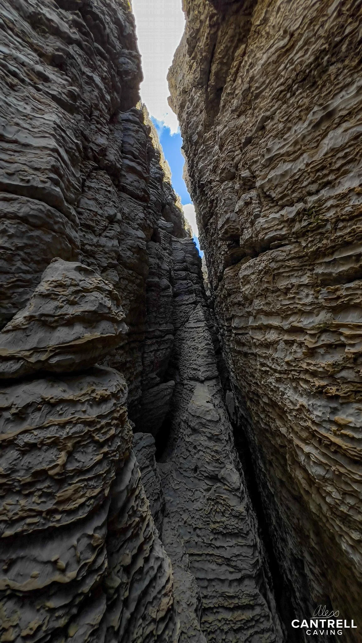 Narrow rock crevasse with layered formations and visible sky above.