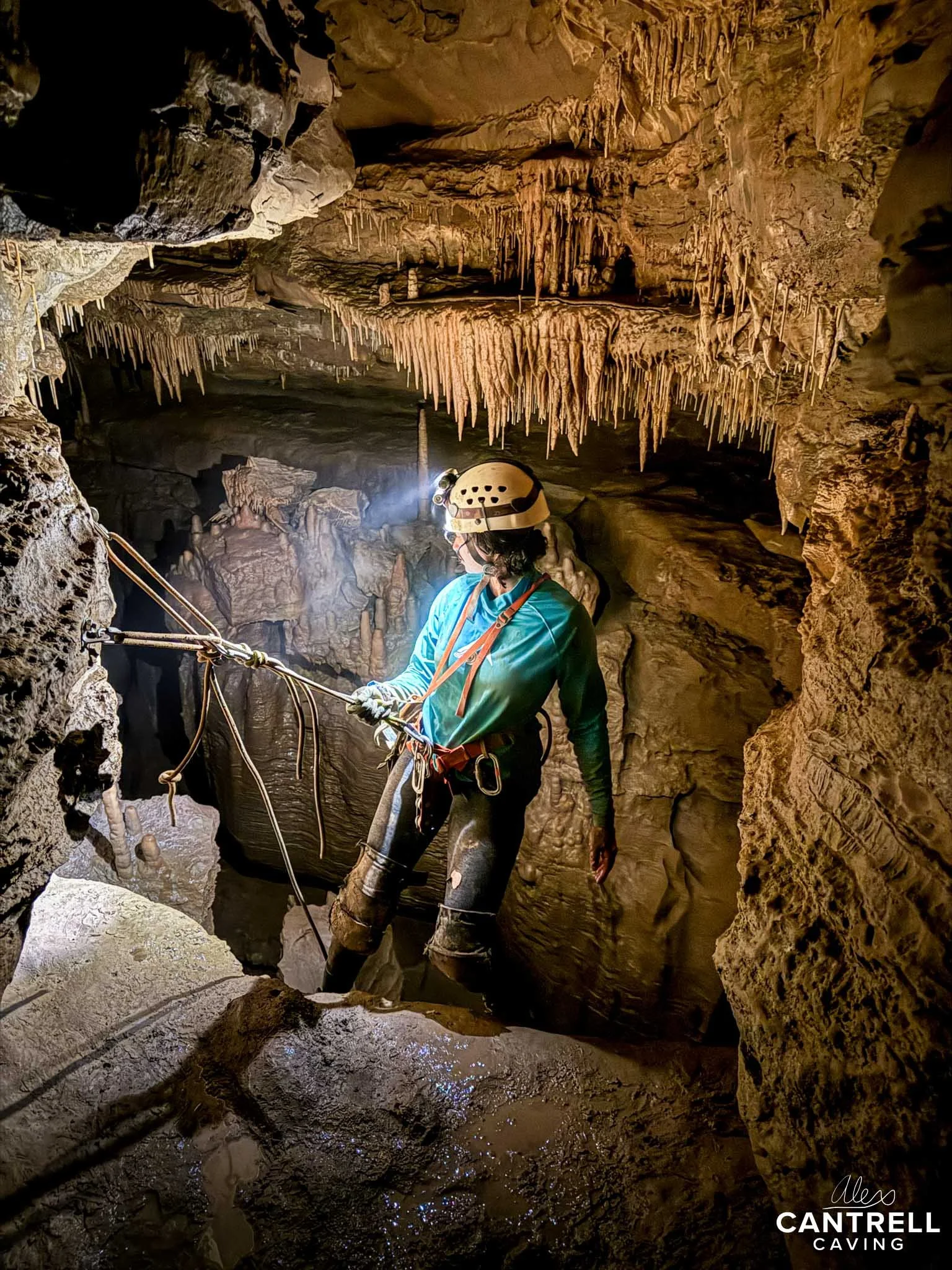 Caver exploring a cave with stalactites visible on the ceiling.