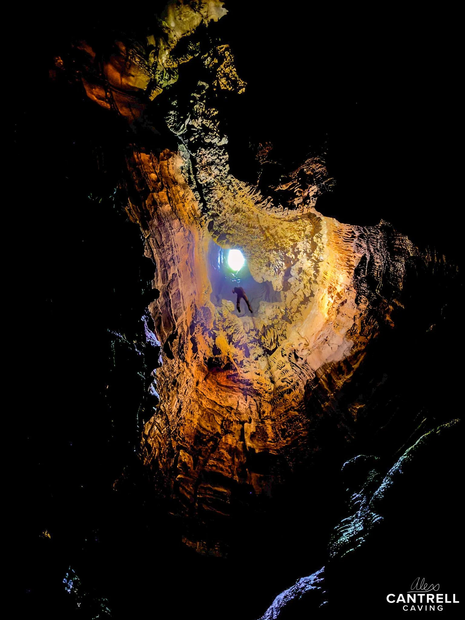 A person descending into a deep cave with rocky walls, illuminated by natural light from an opening above.