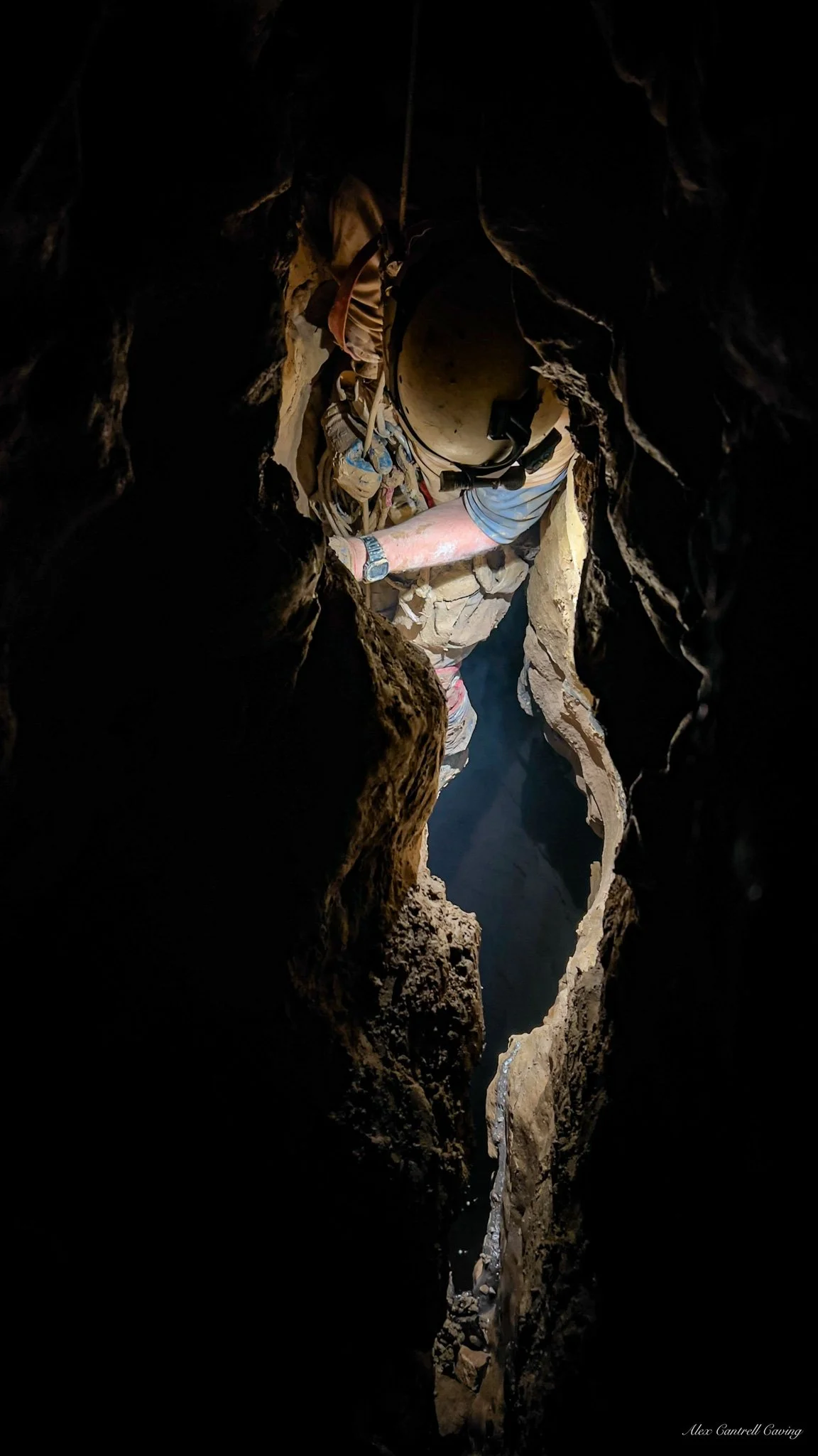 Caver exploring a narrow cave passage with helmet and headlamp.