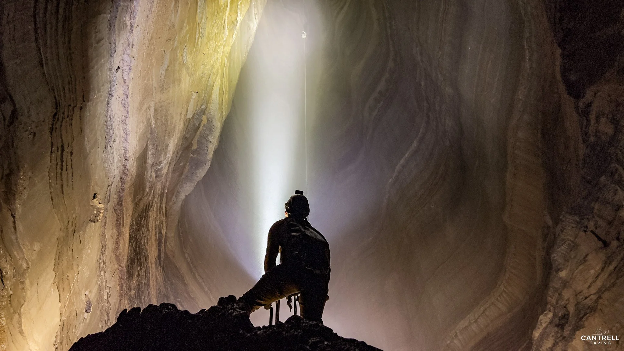 Person caving inside a large rocky chamber with flashlight.