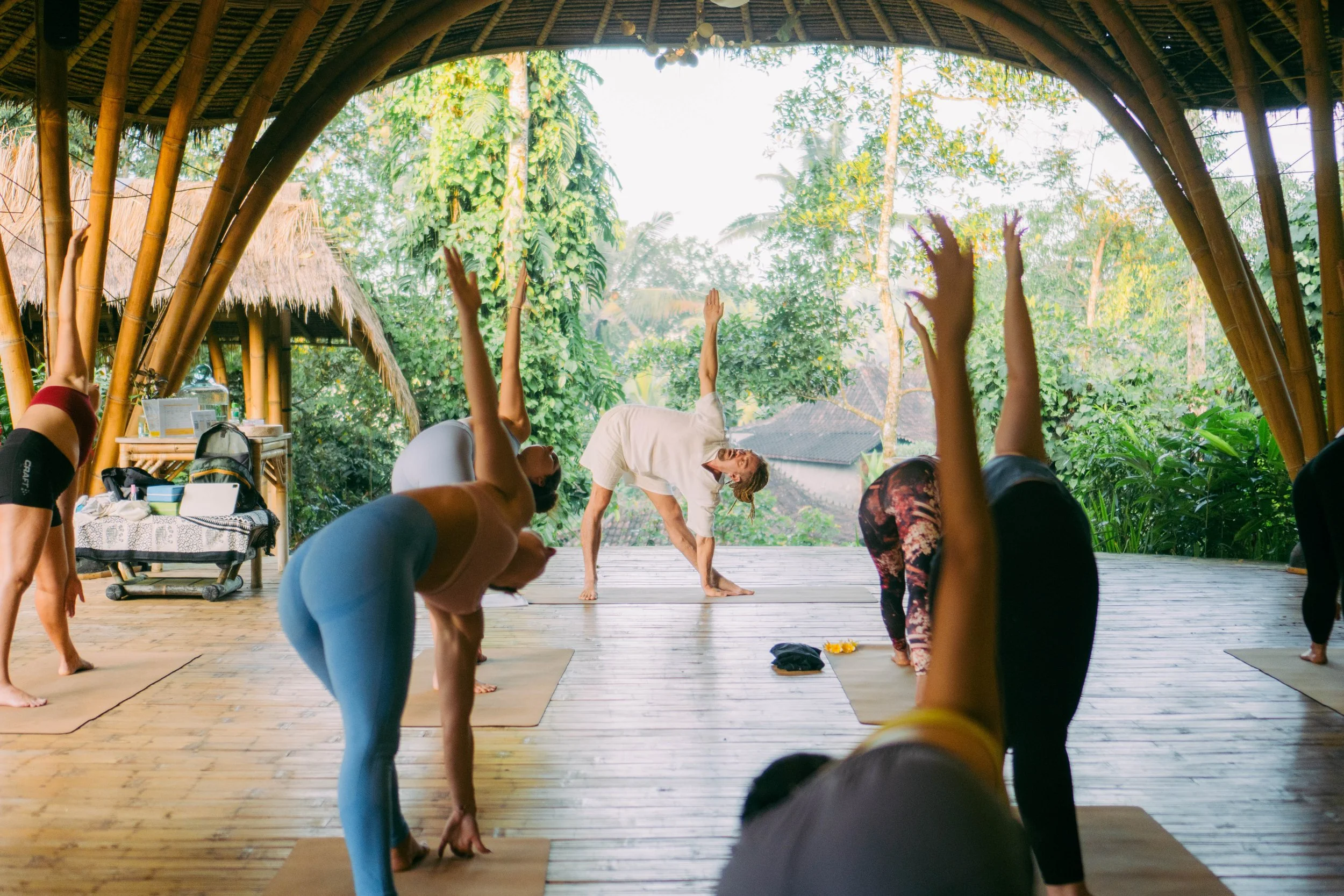 Students practising advanced Hatha Yoga asanas in the natural light of the bamboo shala at SKY Yoga and Meditation Bali
