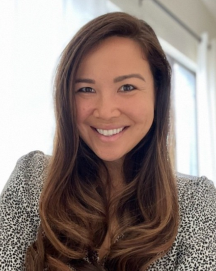 A woman with long, wavy hair smiling at the camera in an indoor setting.