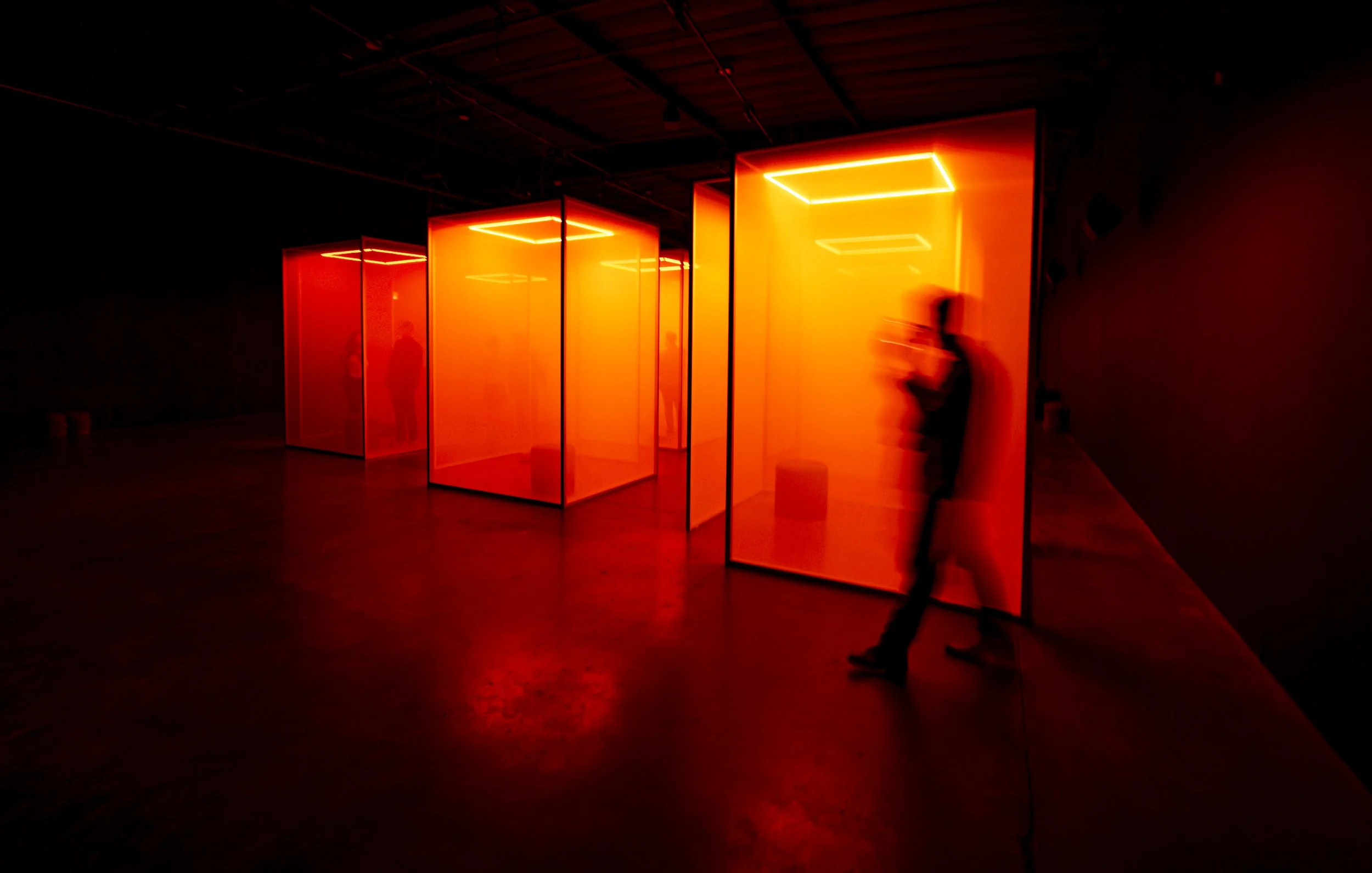 People observing an art installation with illuminated red and orange glowing panels in a dark gallery space.
