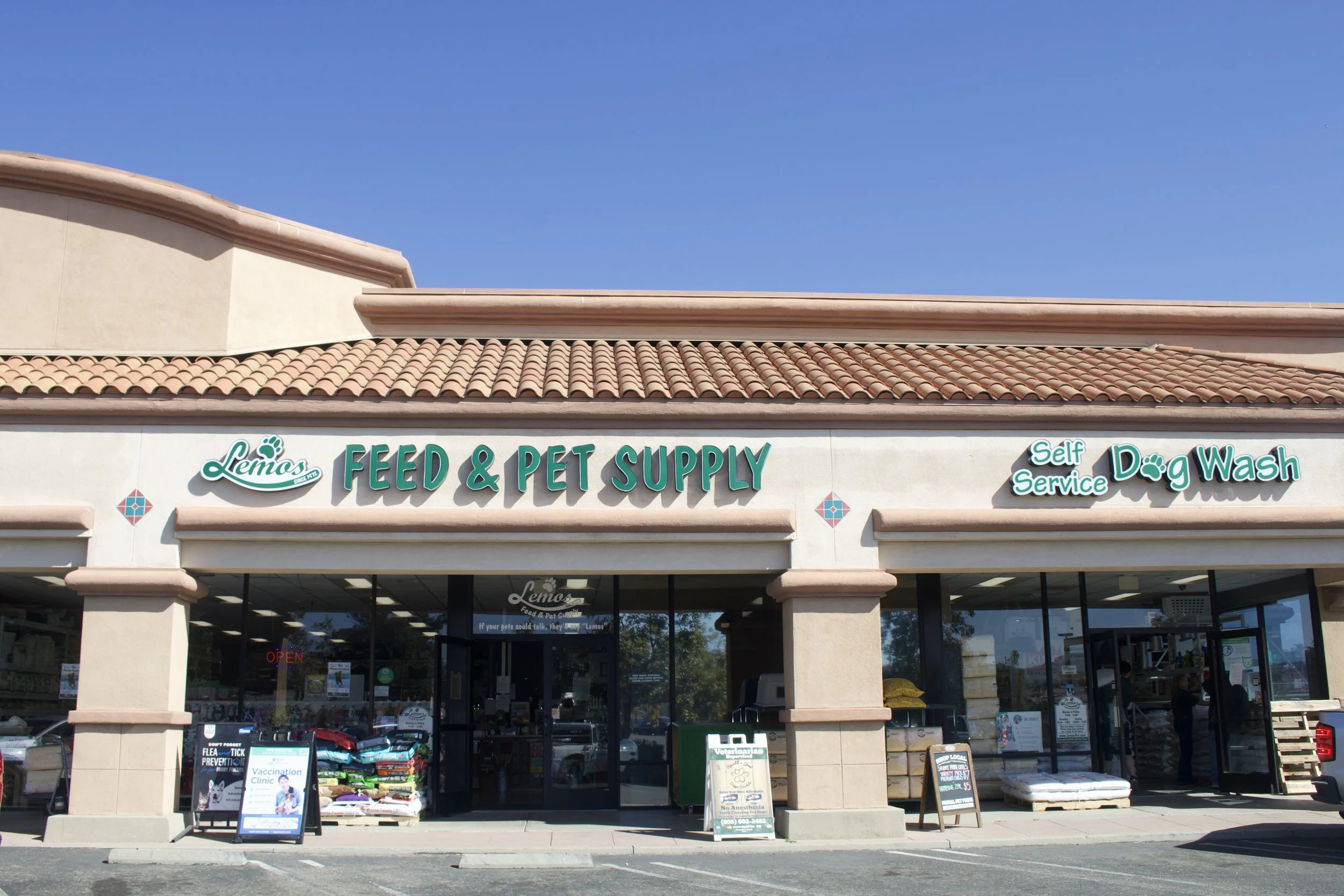 Exterior view of Lemos Feed & Pet Supply in Lompoc with a beige stucco facade, a clay tile roof, and large glass windows at the entrance.