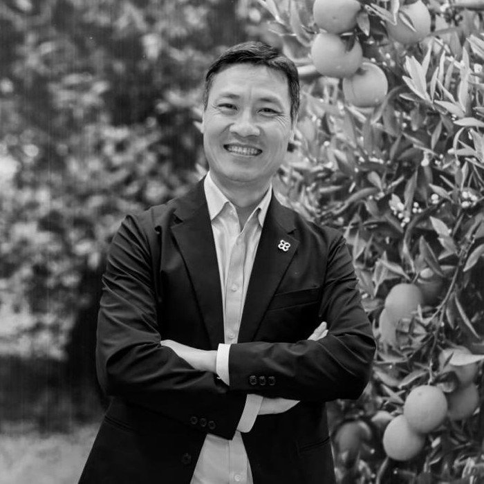 A smiling man in a suit with his arms crossed standing near an orange farm.
