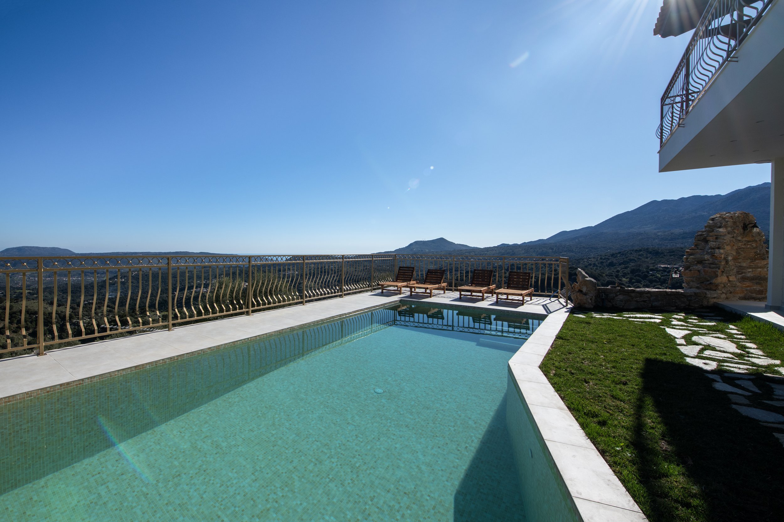 Outdoor swimming pool with lounge chairs and mountains in the background under a clear blue sky.