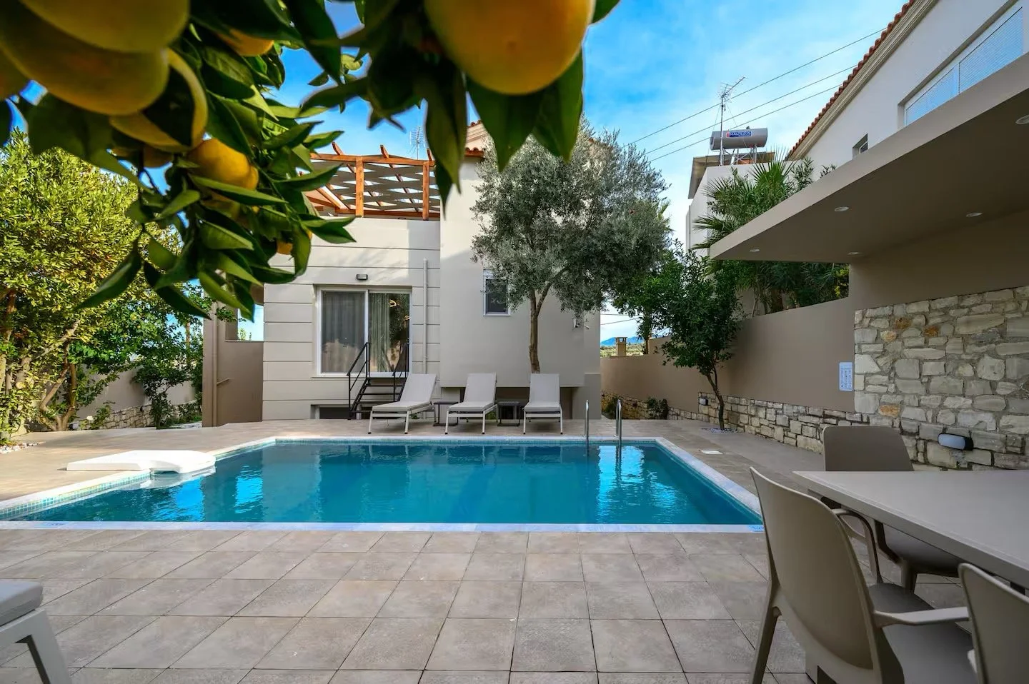 Poolside backyard with a swimming pool, lounge chairs, trees, and a villa-style house.