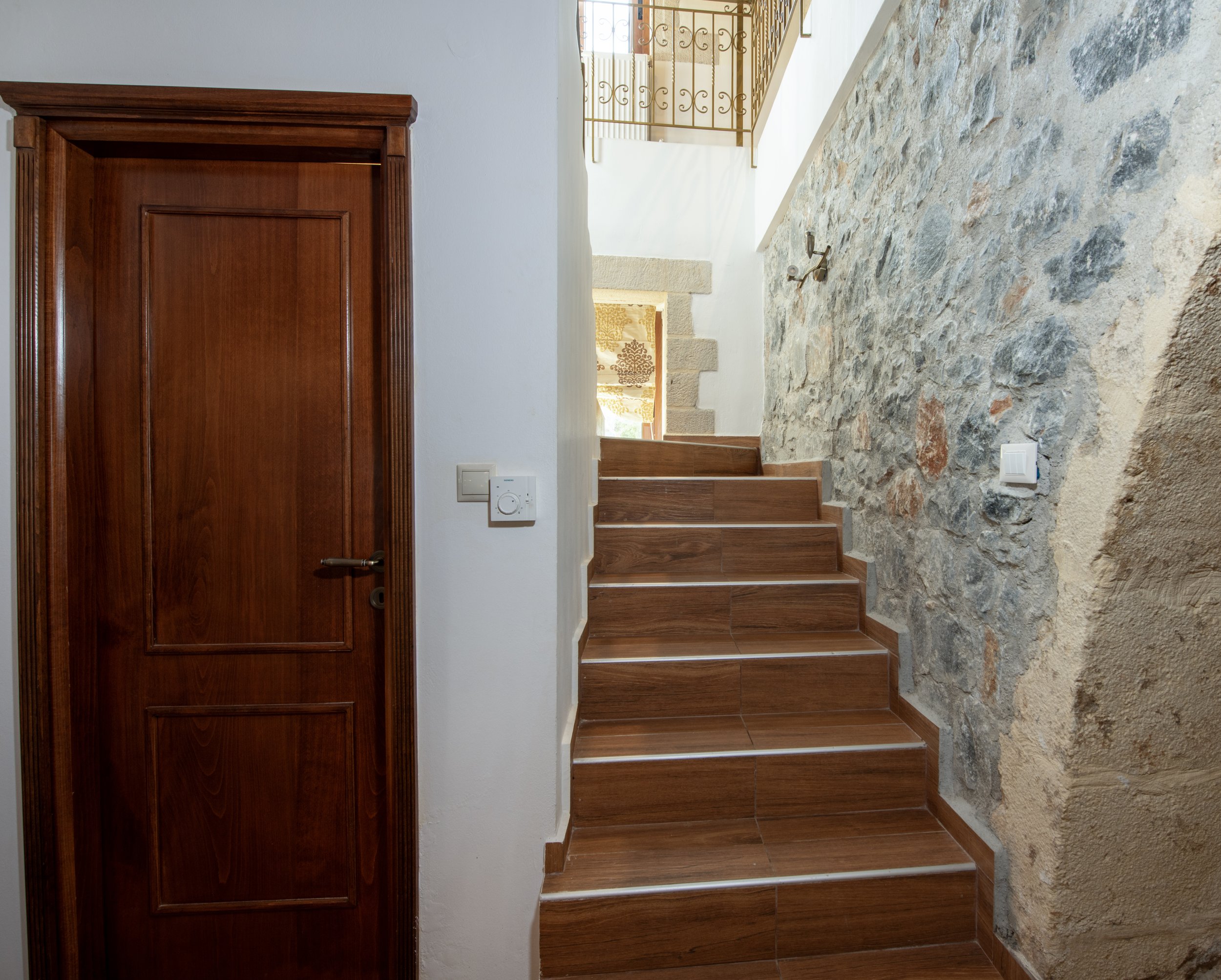 Wooden staircase with stone wall, wooden door, and decorative railing.
