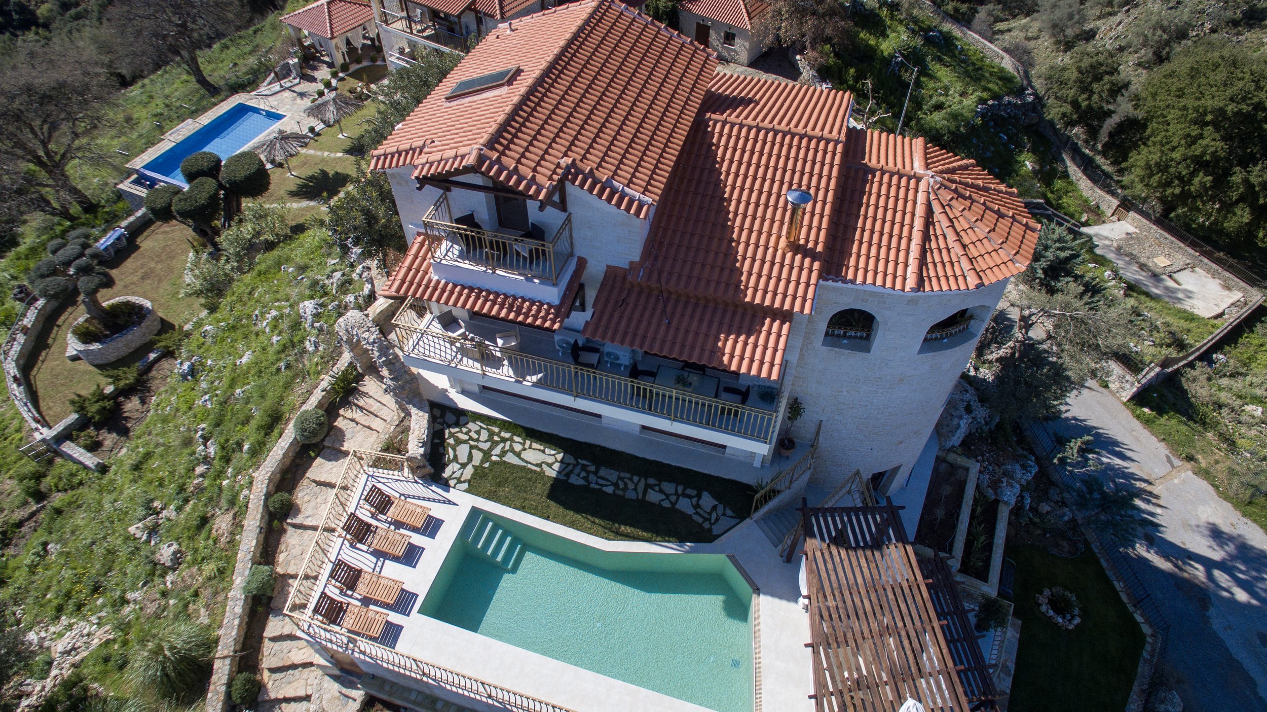 Aerial view of a large house with red tile roofs, a swimming pool, and landscaped gardens.