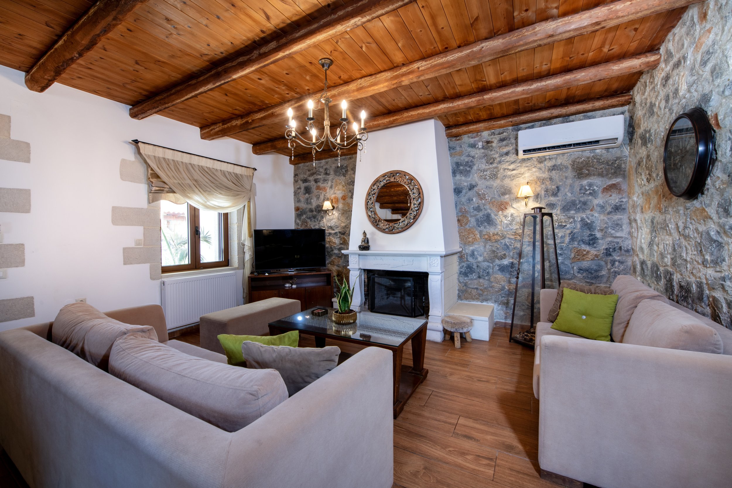 Cozy living room with beige sofas, wooden ceiling, stone walls, fireplace, and TV