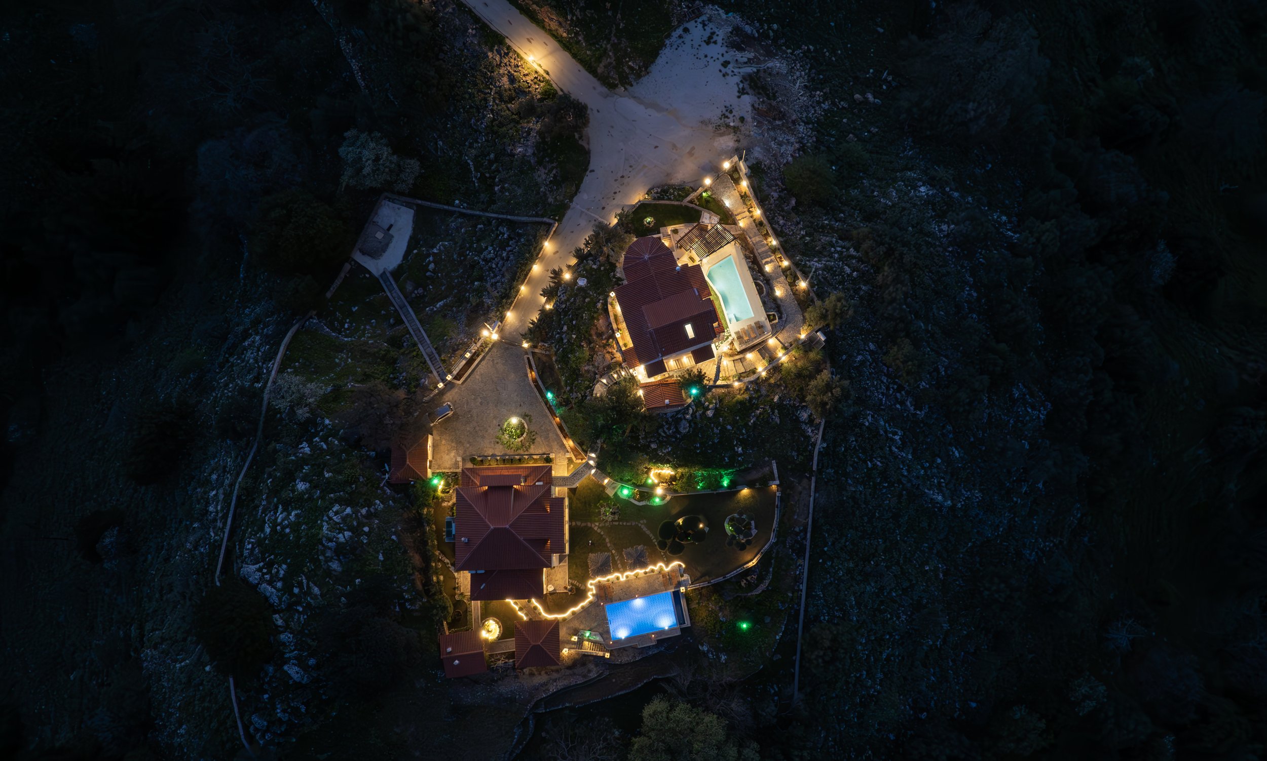 Aerial view of illuminated buildings and pools in a mountainous area at night.