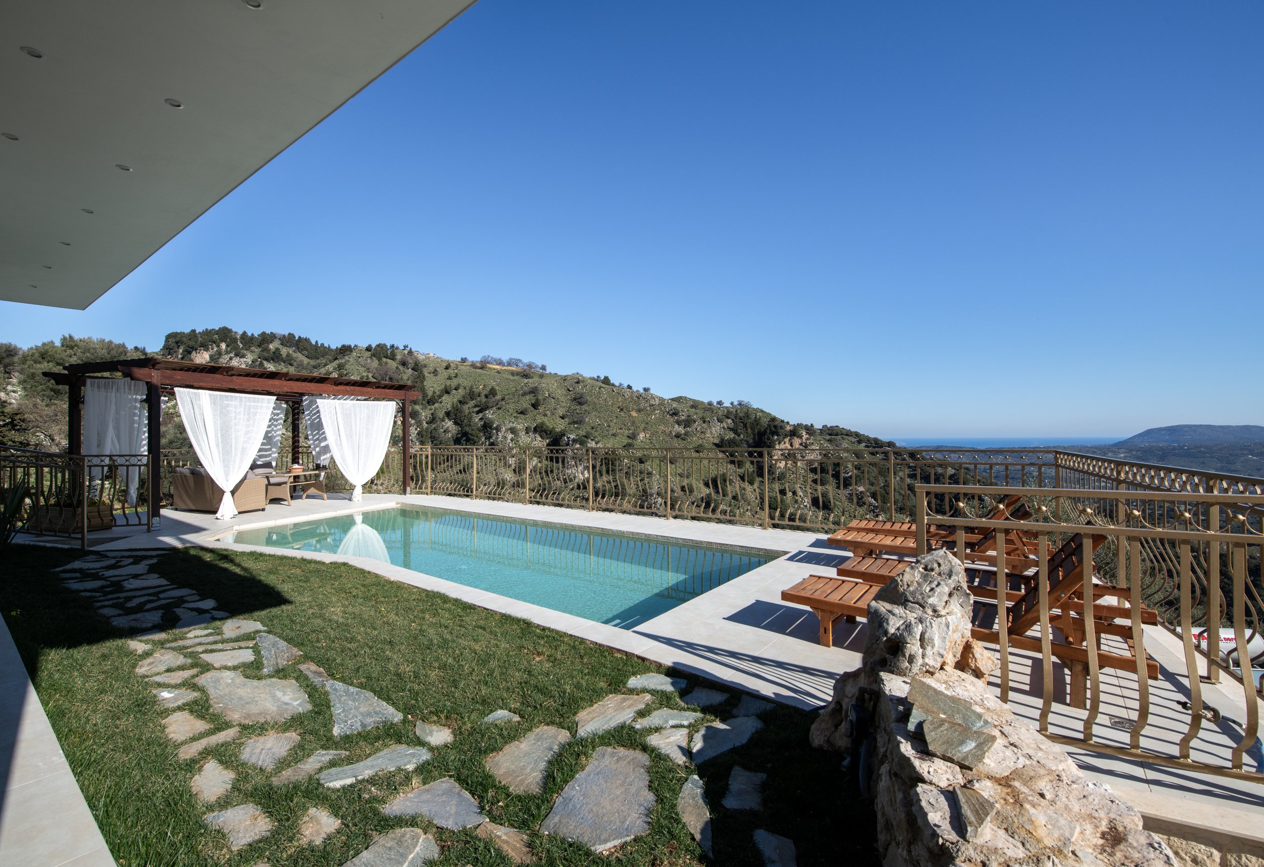 Outdoor swimming pool with a pergola and loungers overlooking a scenic mountain landscape.
