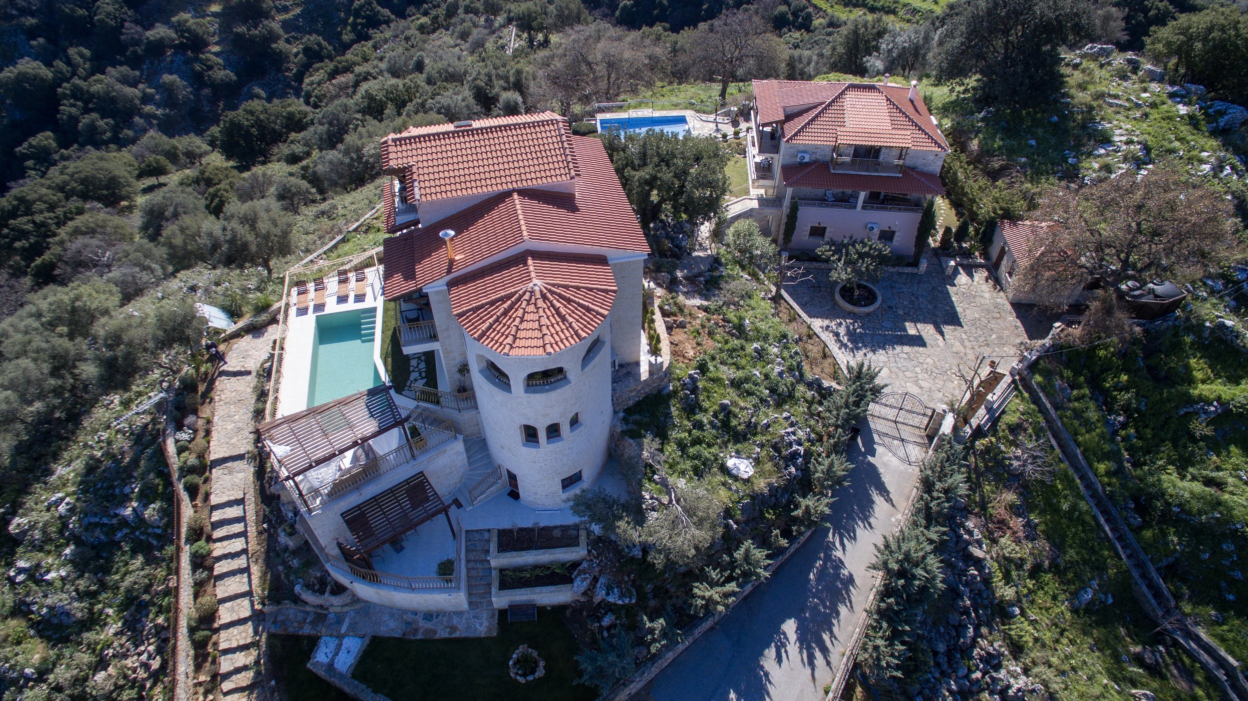 Aerial view of a luxury villa with a swimming pool and garden, surrounded by lush greenery and trees.