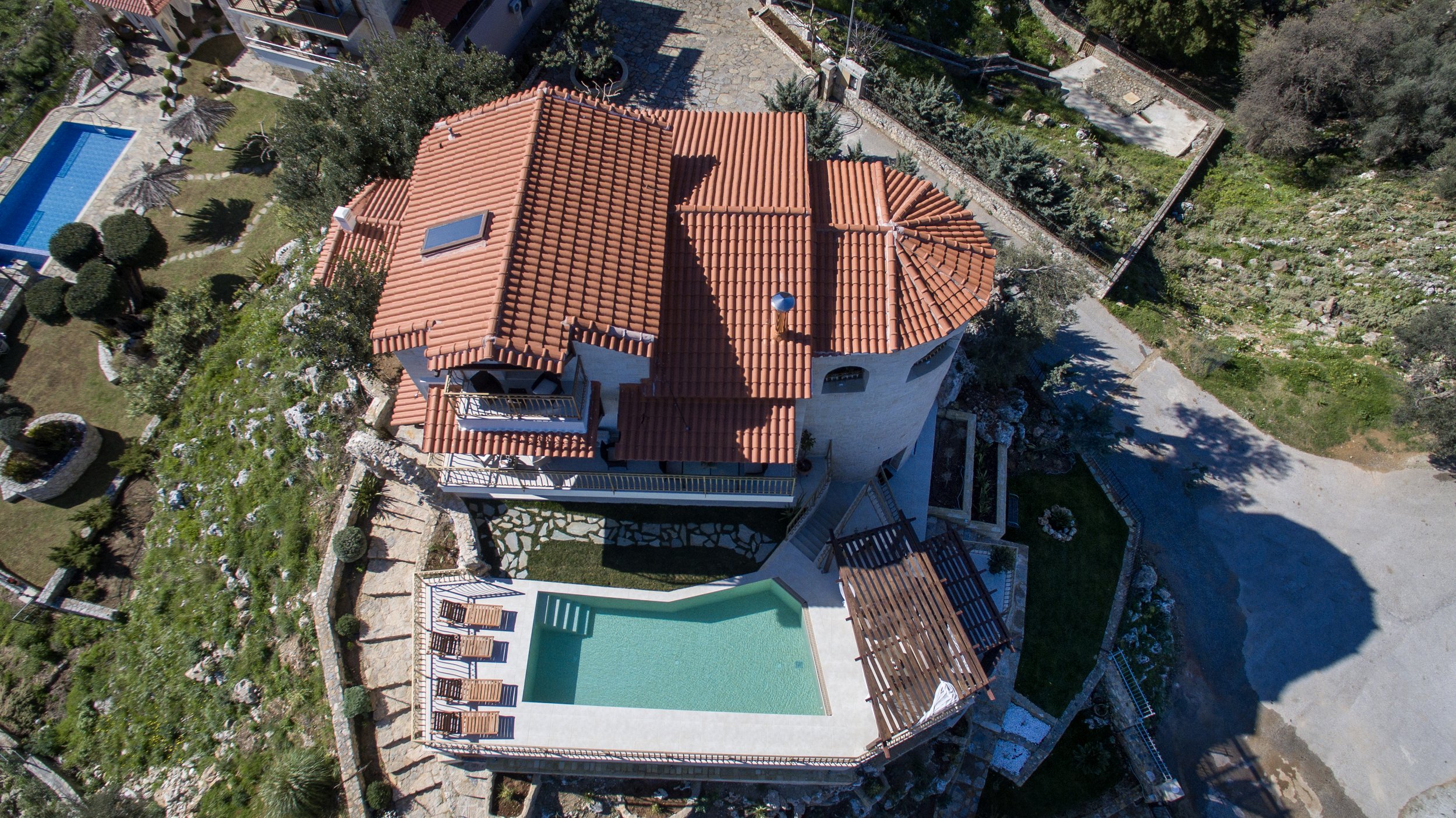 Aerial view of a Mediterranean-style house with red tile roof, surrounded by a garden and a swimming pool with sun loungers.