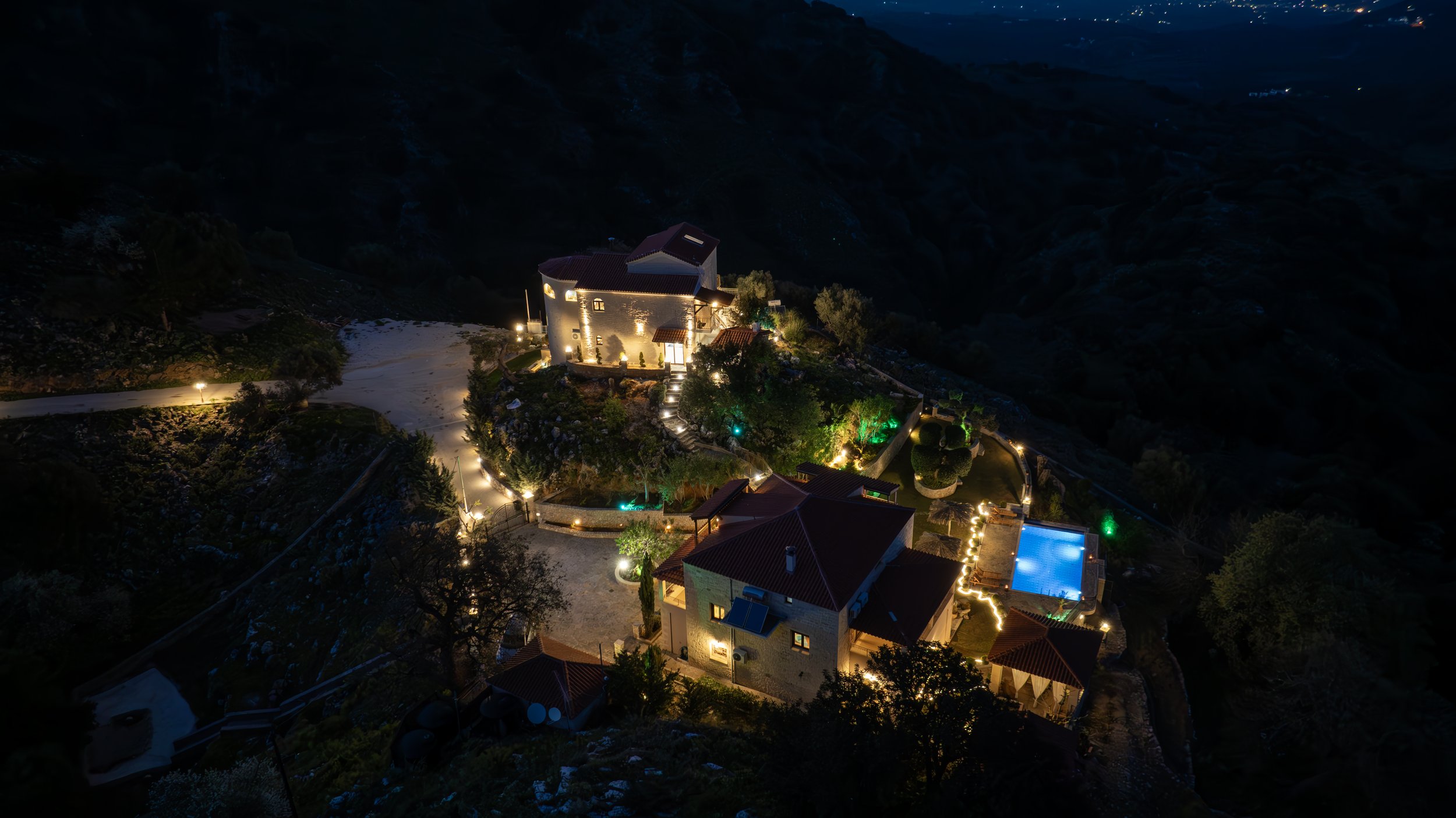 Aerial view of illuminated houses and a swimming pool on a hillside at night.