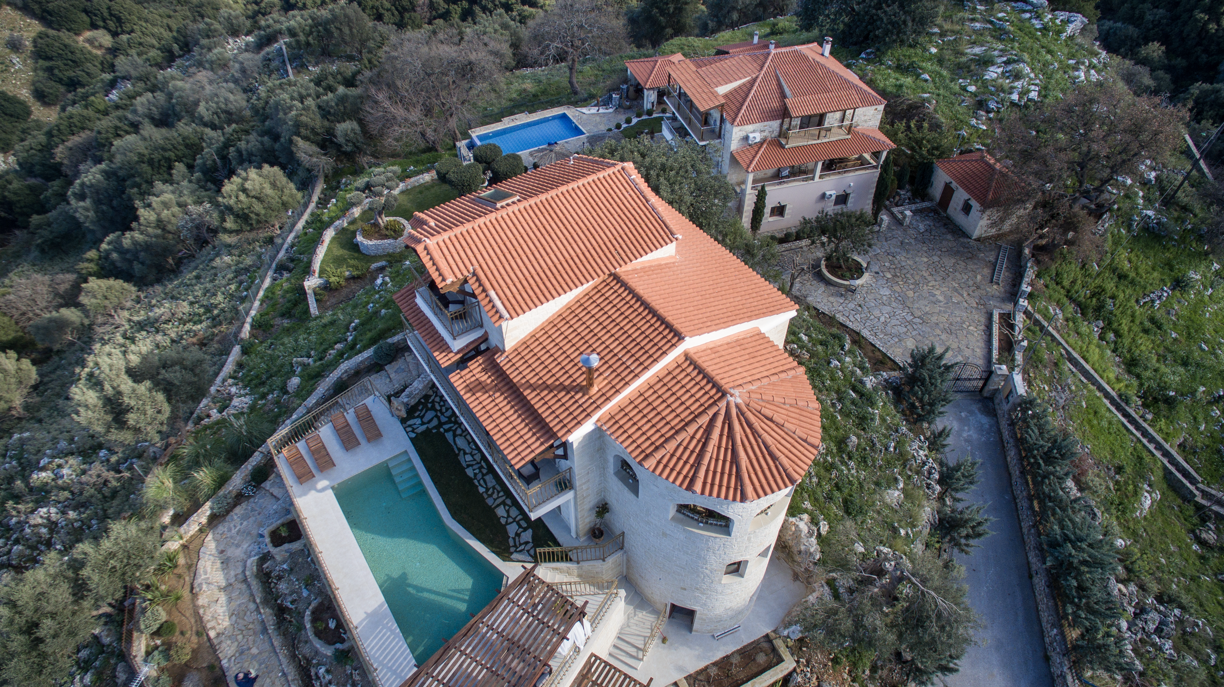 Aerial view of a Mediterranean-style villa with red-tiled roofs, multiple levels, a swimming pool, and surrounding greenery.