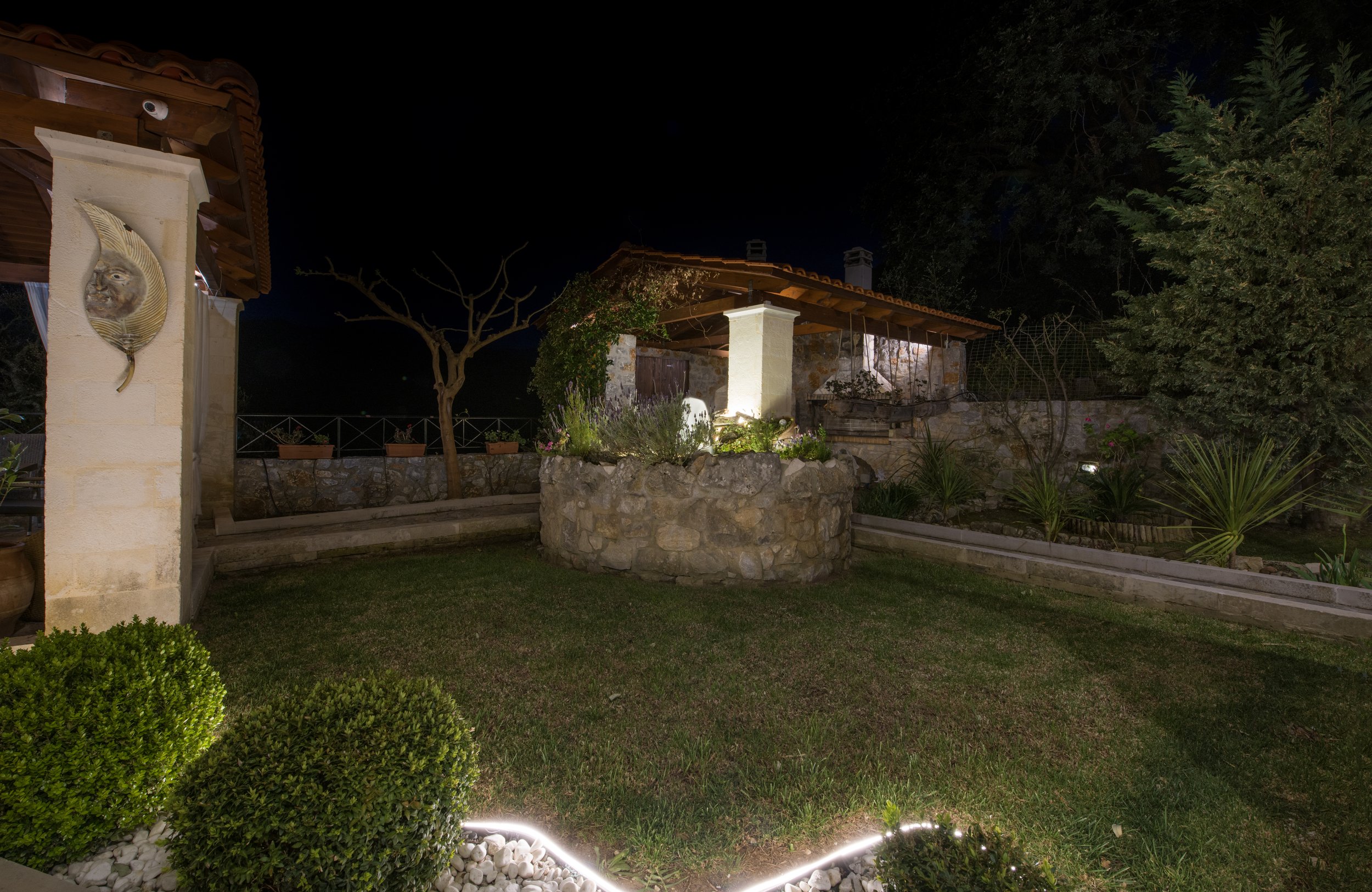 Night garden with stone structure, illuminated plants, and small outdoor building