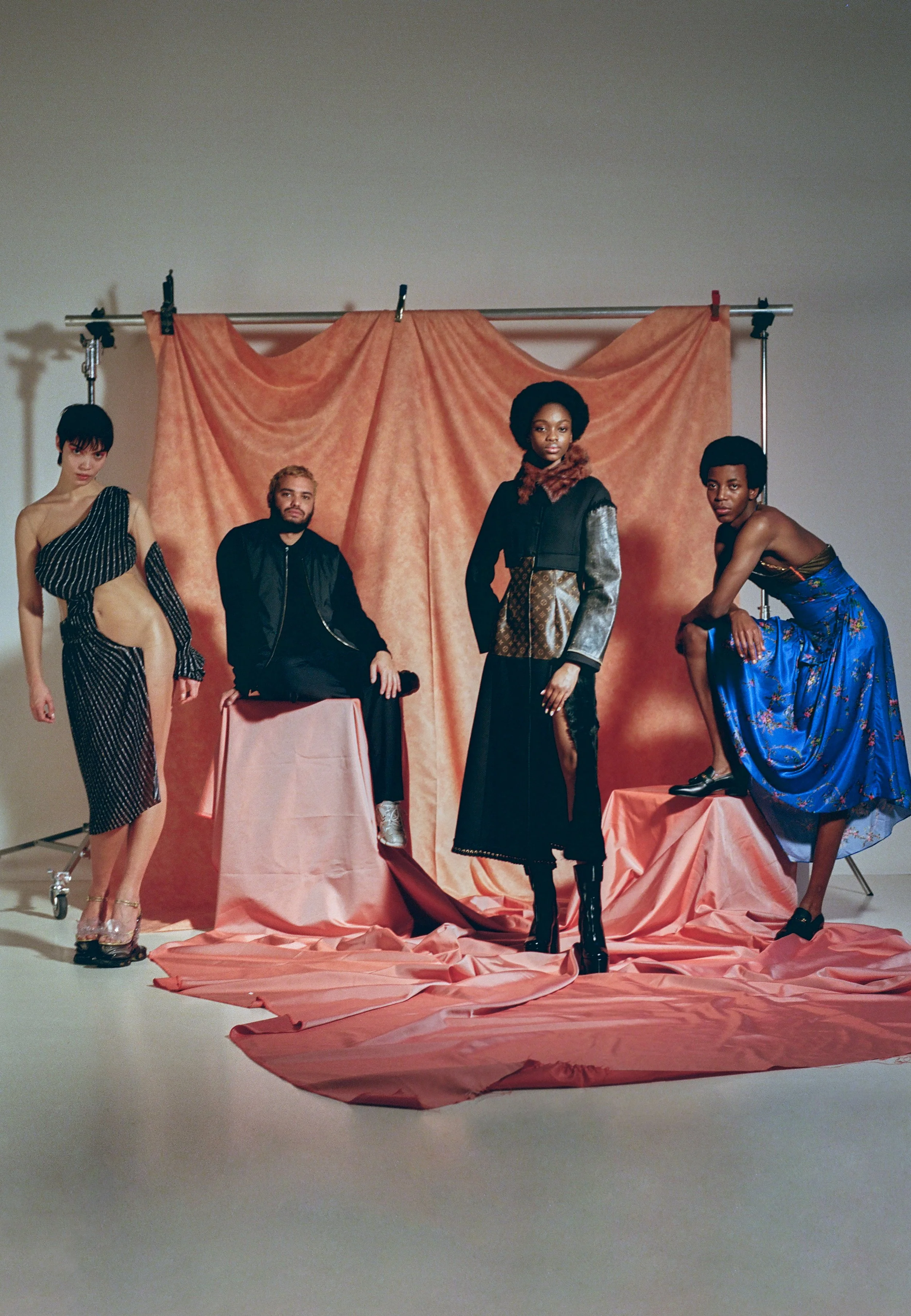Four models posing in fashion outfits against a peach-colored backdrop in a photo studio.