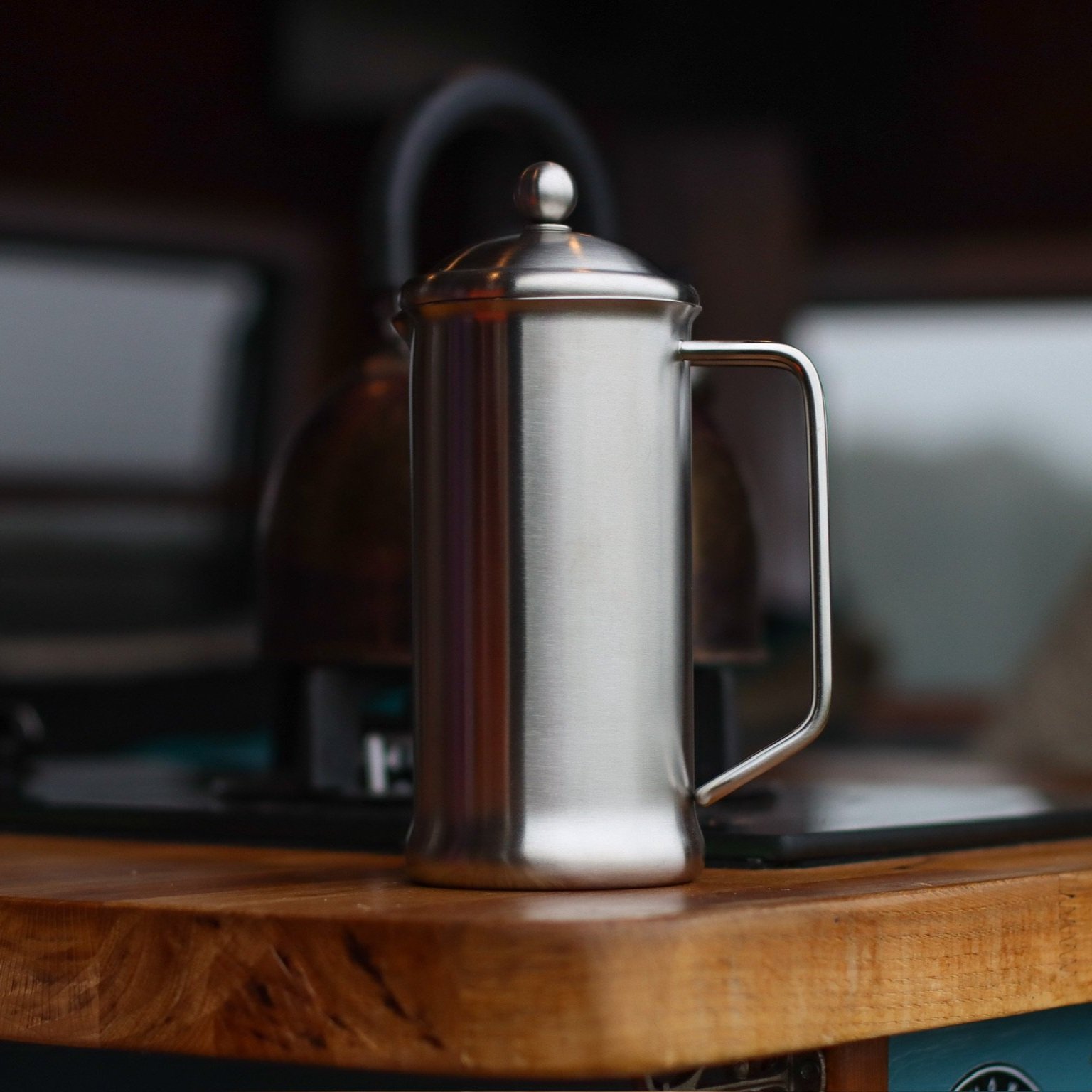 Silver stainless steel cafetiere shown on wooden countertop with hob and kettle behind