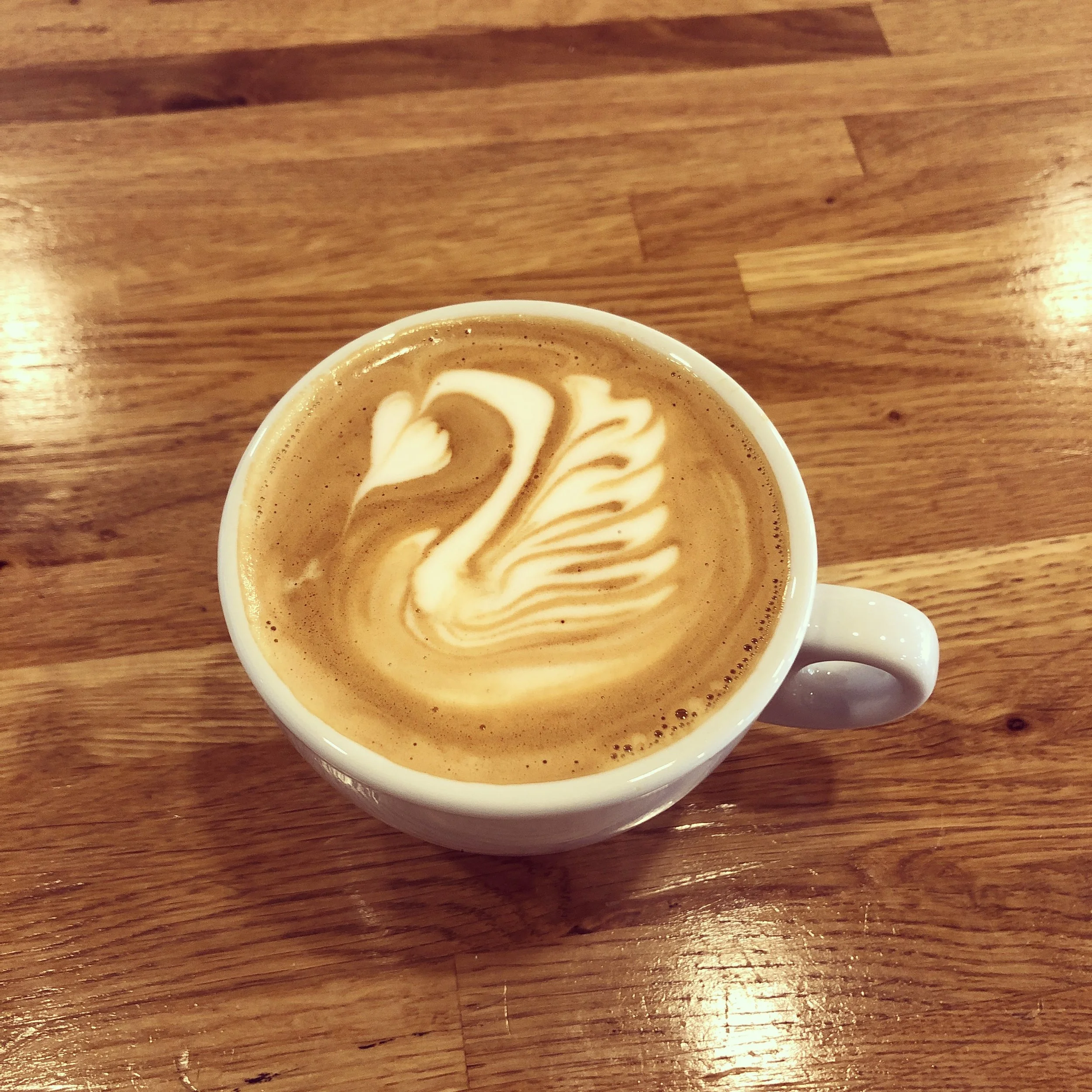Latte art swan shown on coffee in white mug on a wooden counter