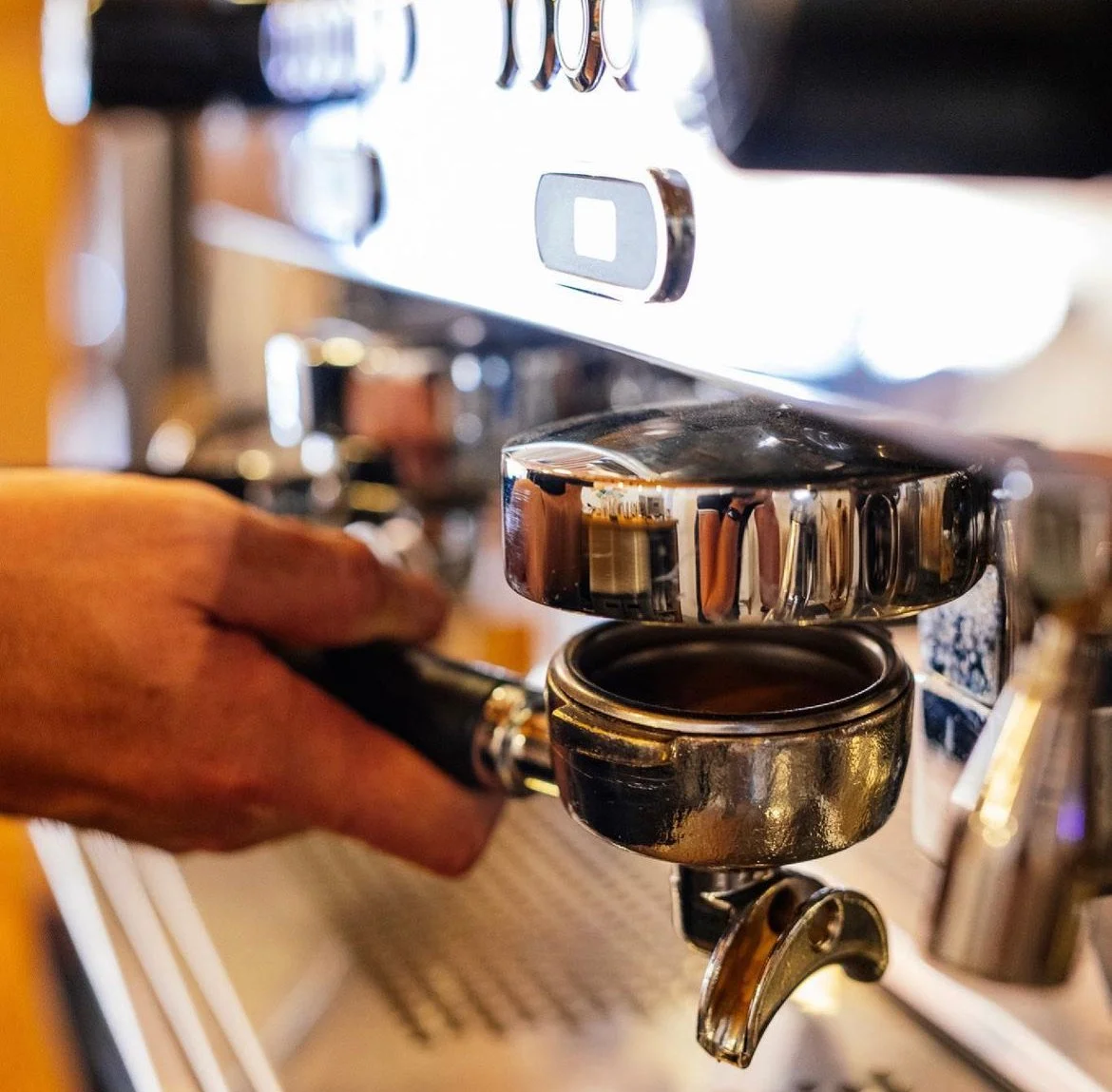 Close up of hand shown operating a coffee machine in coffee shop