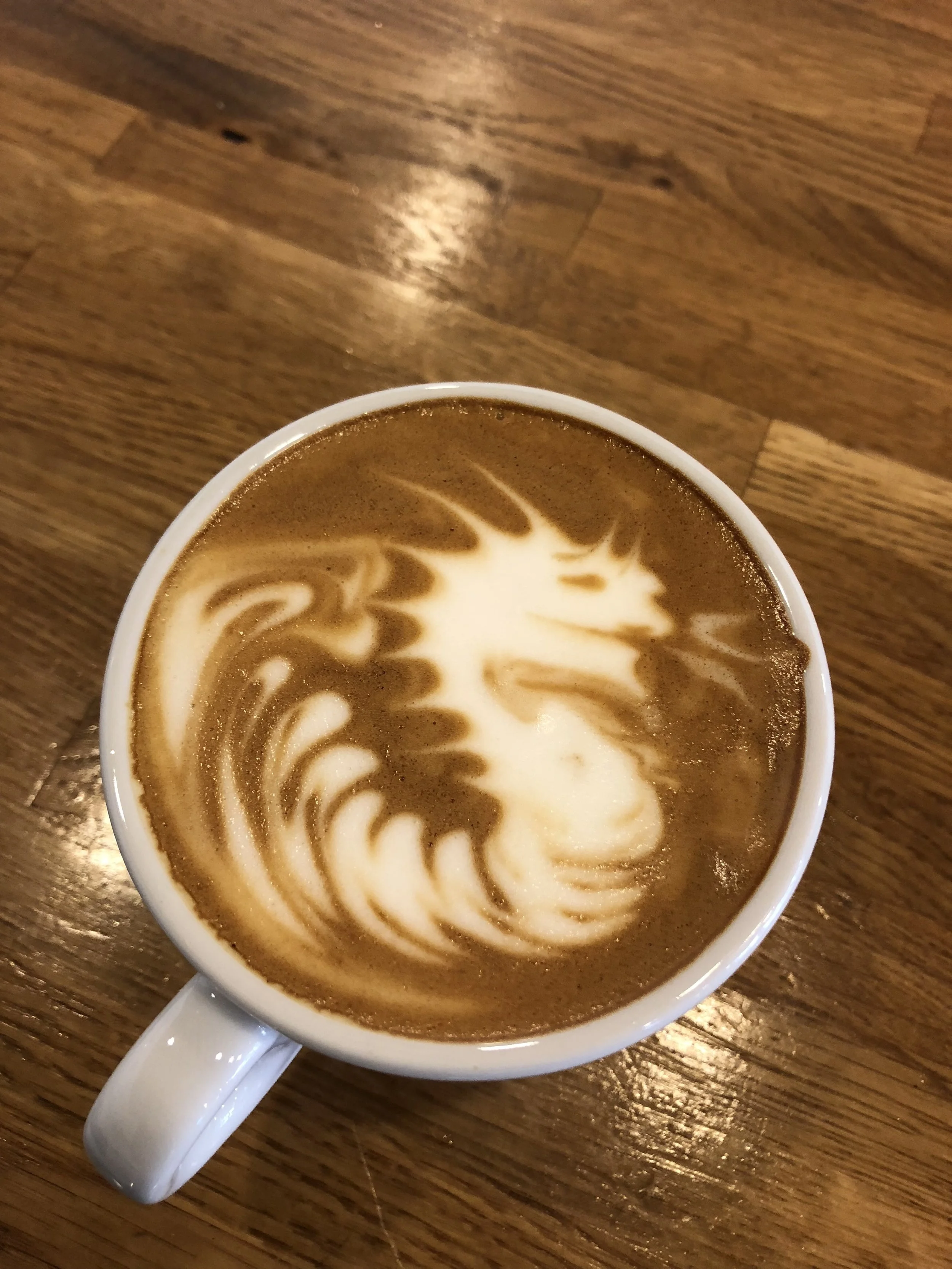 Latte art dragon shown on coffee in white mug on a wooden counter