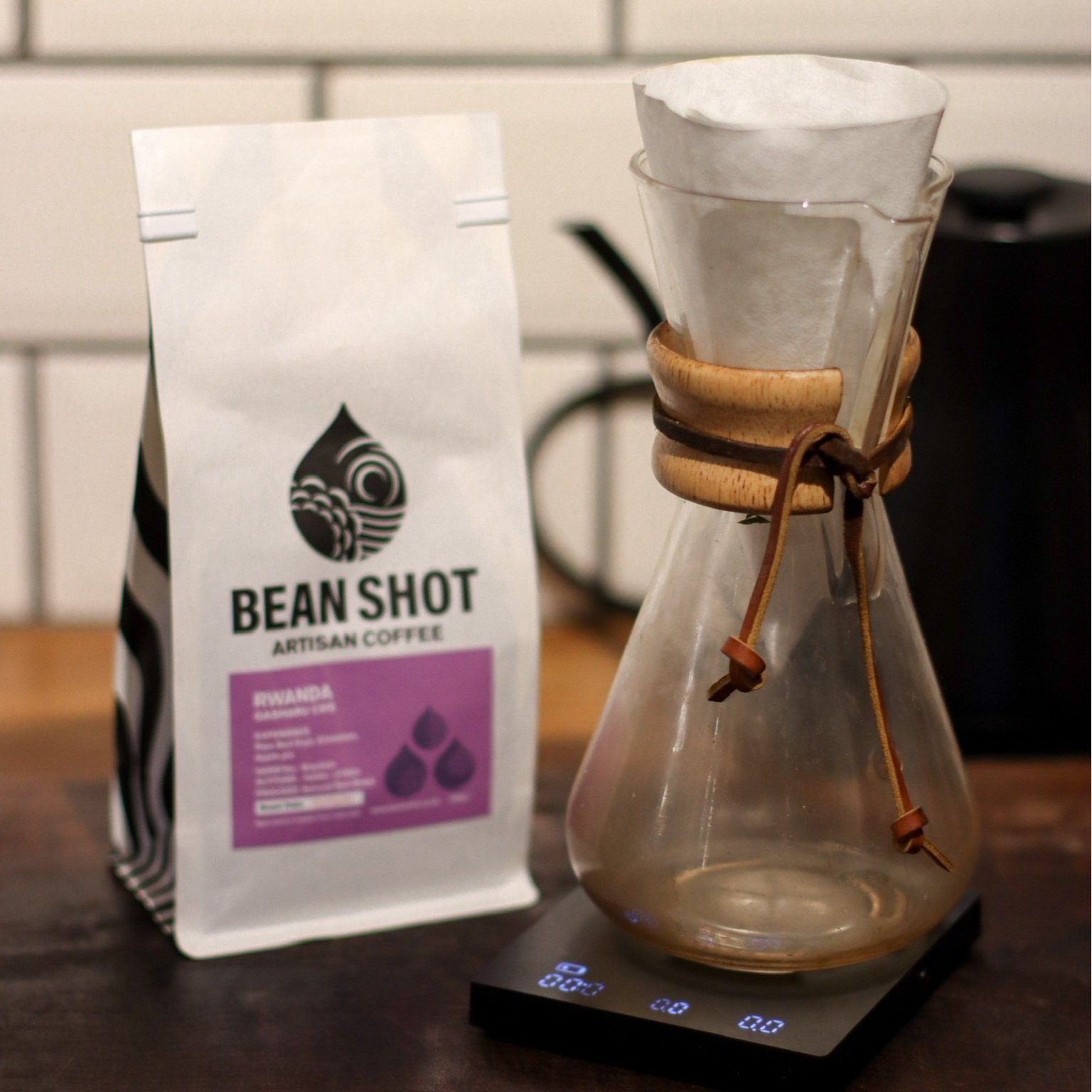 Chemex 6 cup pour over coffee maker shown in kitchen on scales with coffee brewing and bag of bean shot coffee behind