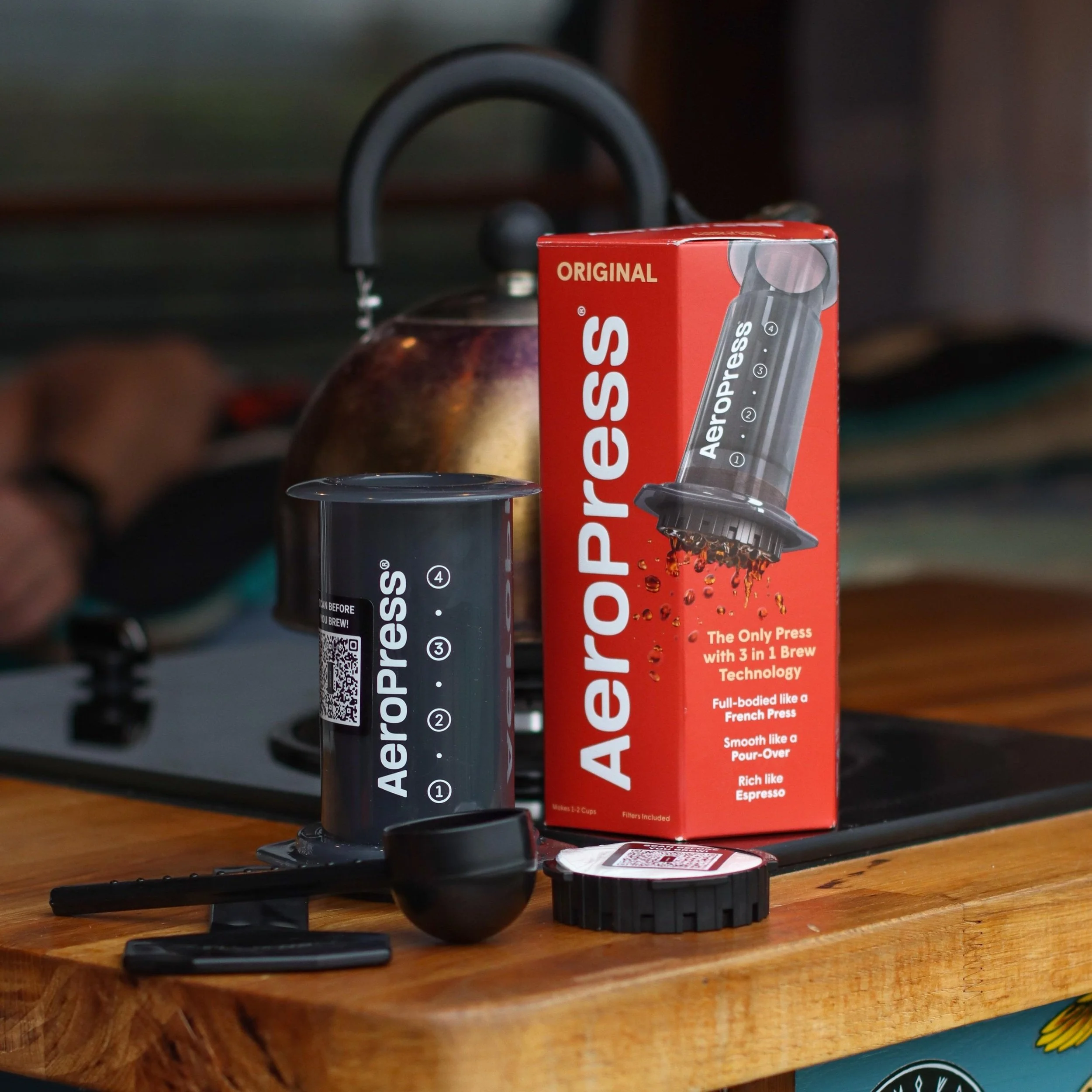 Aeropress shown next to packaging on wooden counter with hob and kettle behind