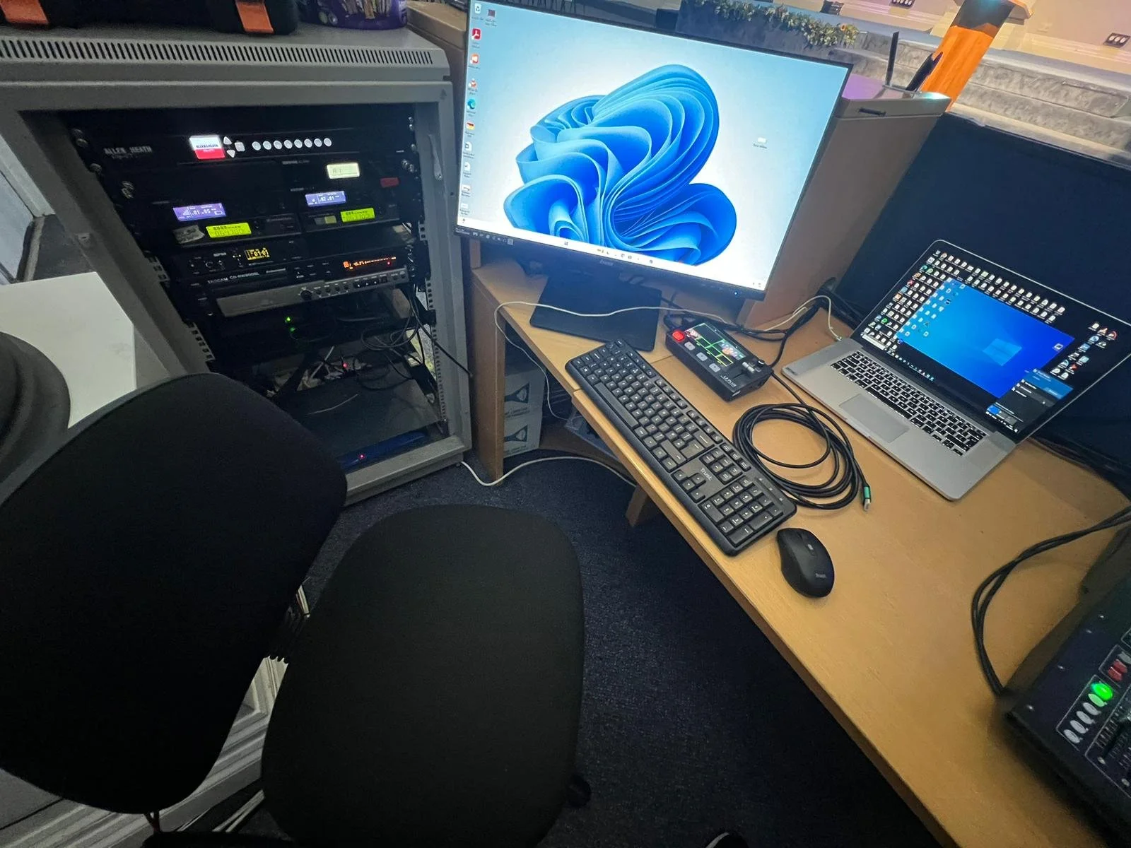 Office setup with computer monitor, laptop, keyboard, and server rack