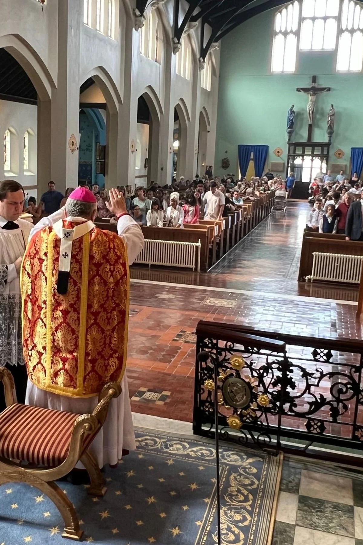 A bishop wearing ornate vestments leads a church service in a large cathedral filled with seated congregation; altar in the background.