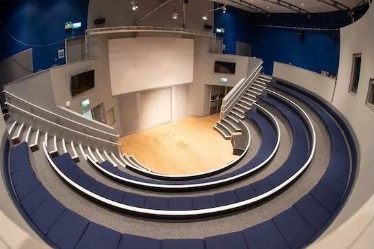 Modern amphitheater with curved seating, blue accents, and a central stage area.