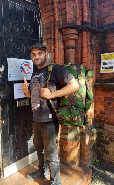 A homeless man standing with his shelterbag, provided by Sheltersuit UK