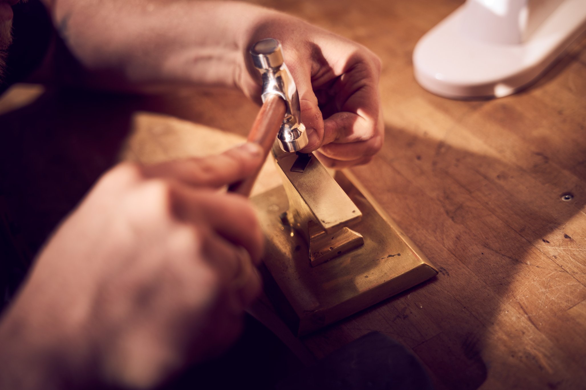 smykkedesigner former guld på ambolt som del af smykkeprocessen