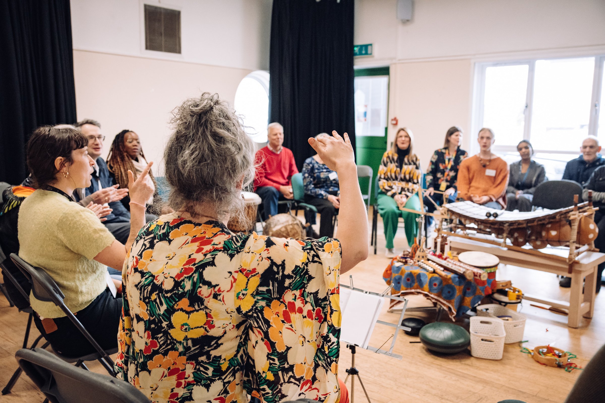 People sitting in a circle, with musical instruments in the centre, enjoying music together.