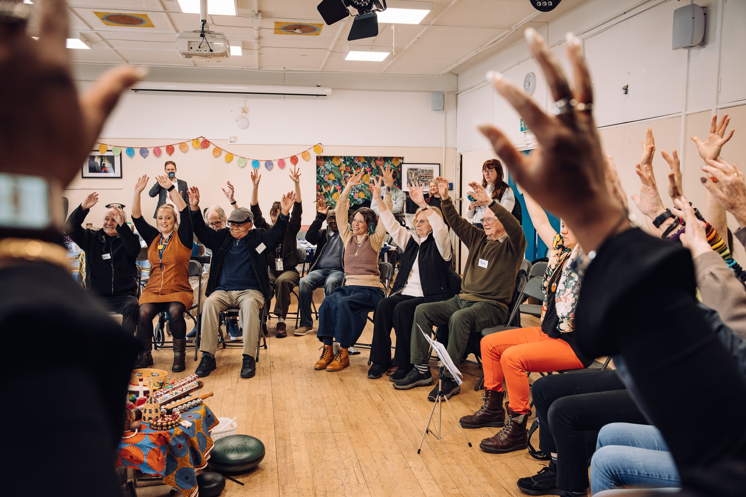 A group of people sitting in a circle with their hands in the air, sharing in music and movement