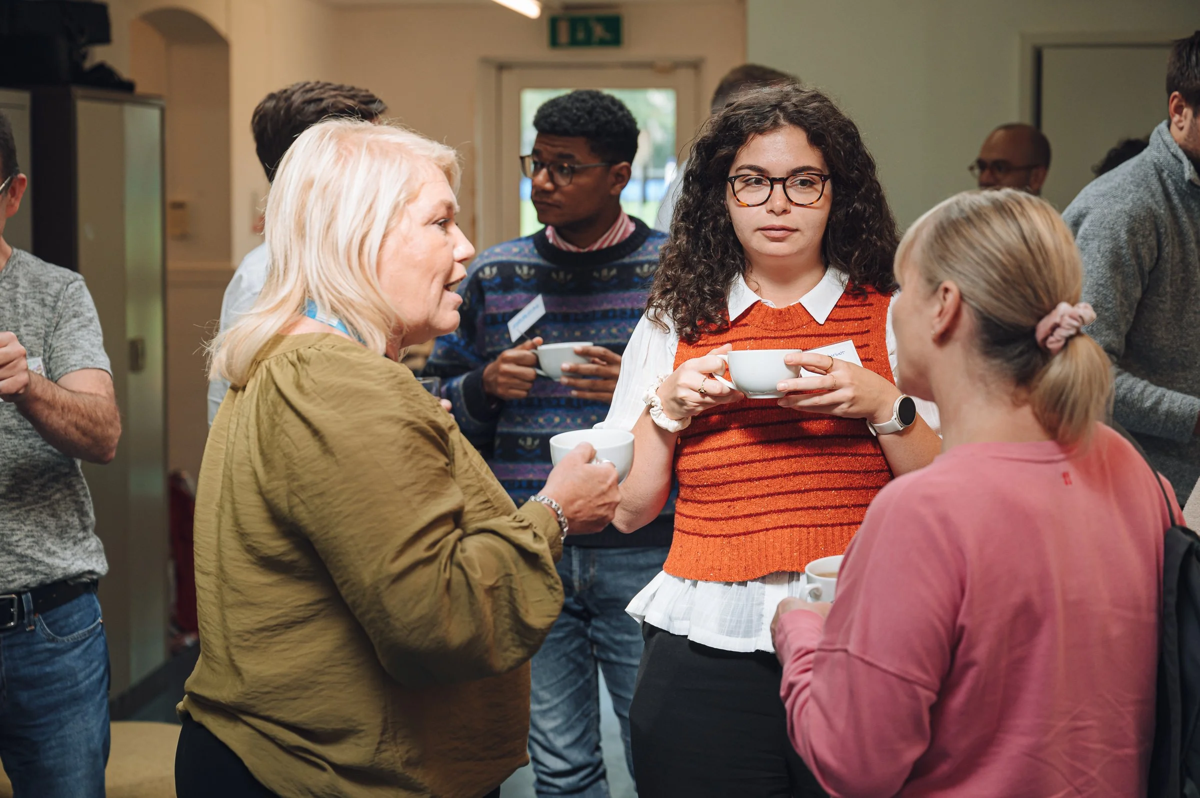 Group of people having a conversation while holding cups at an indoor event.