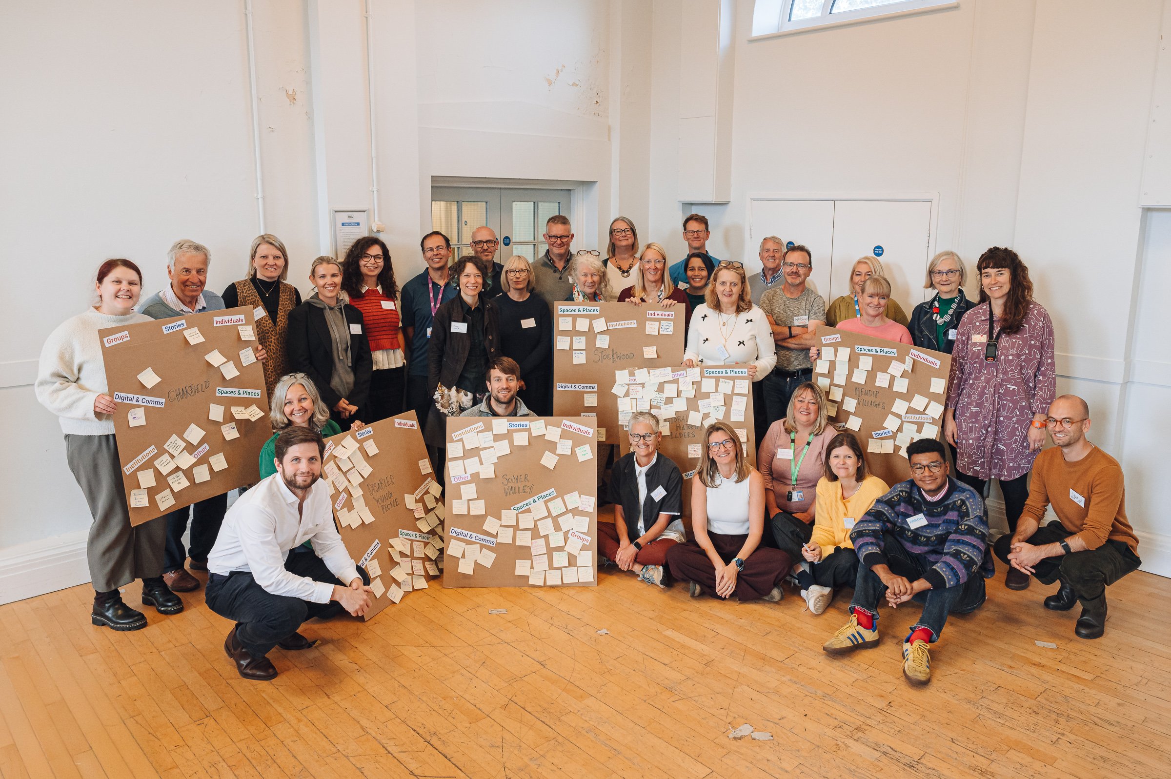 Impact Alliance members at the end of the Enablers' workshop, holding up large boards filled with sticky notes and labels related to topics covered during the day. 