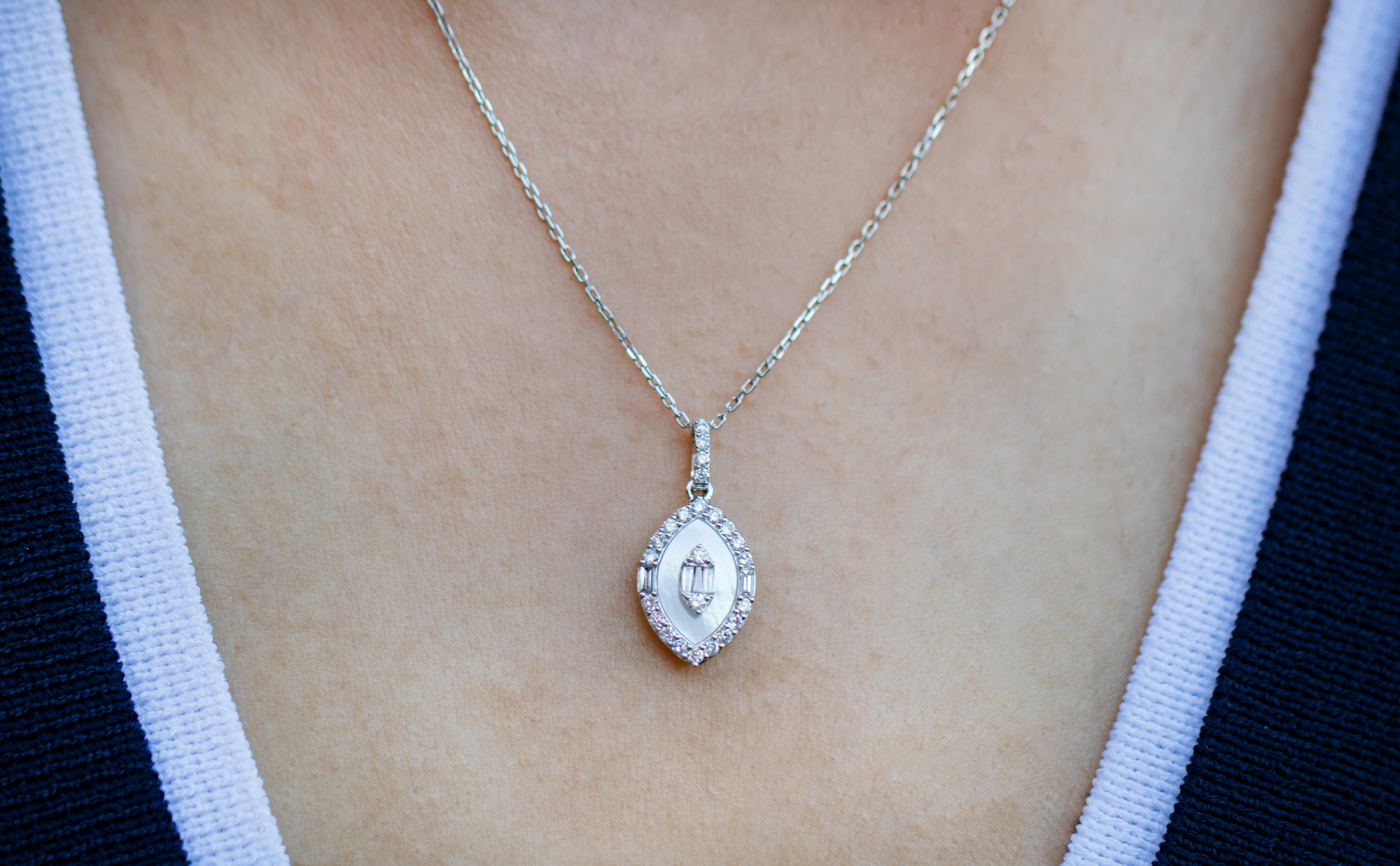 Woman wearing a silver necklace with a teardrop-shaped pendant adorned with small diamonds, dressed in a navy and white garment.