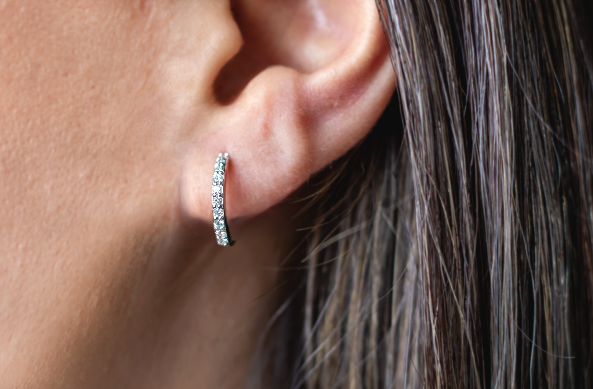 Close-up of a person's ear wearing a small hoop earring with embedded diamonds.