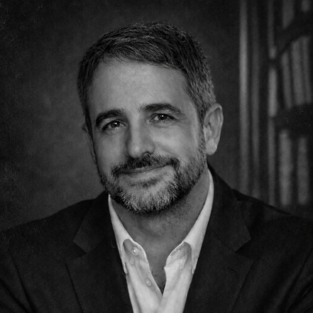 Koyu renk arka plana sahip, takım elbise giymiş, gülümseyen erkek portresi.