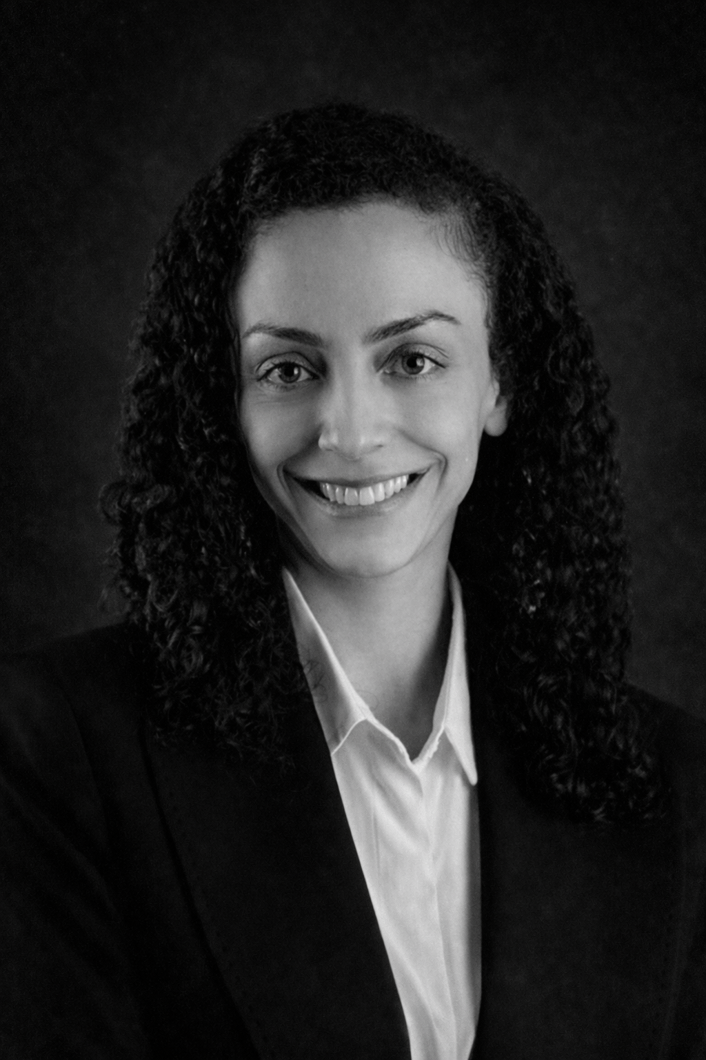 Gülümseyen kadın, açık pembe blazer ve beyaz bluz giymiş, karanlık degrade arka plan