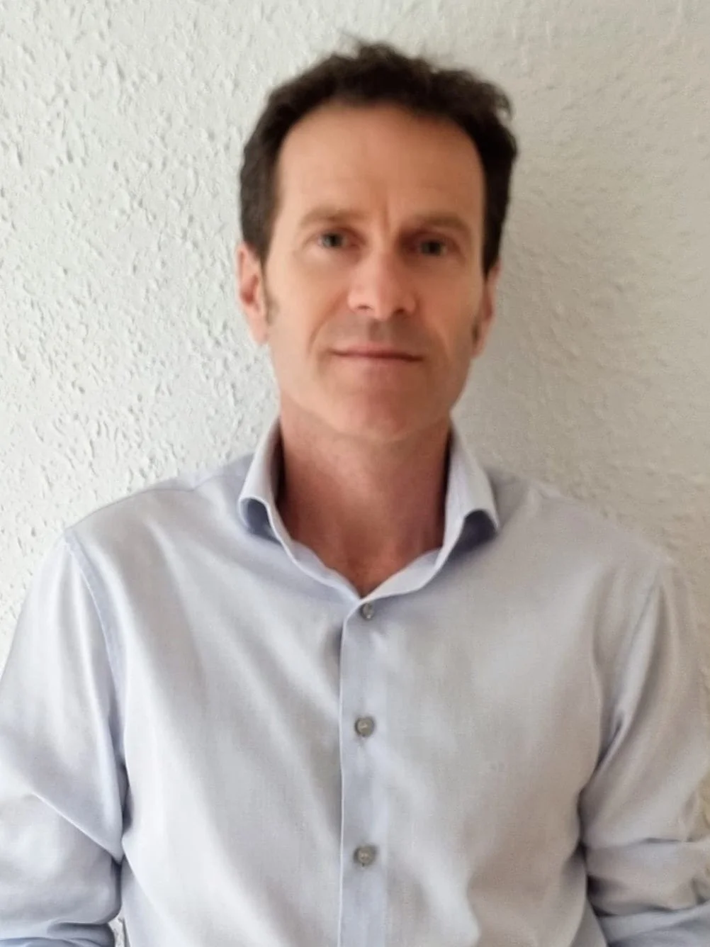 Home de peu amb camisa blanca de botons i fons de paret blanca.