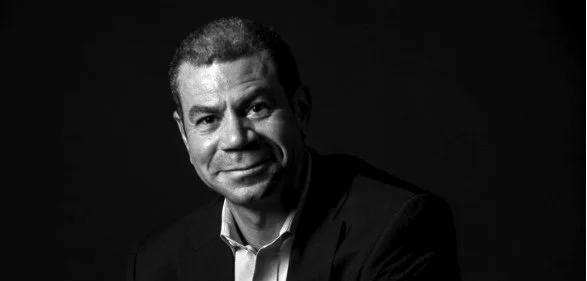 Black and white portrait of a man in a suit, smiling slightly, against a dark background.