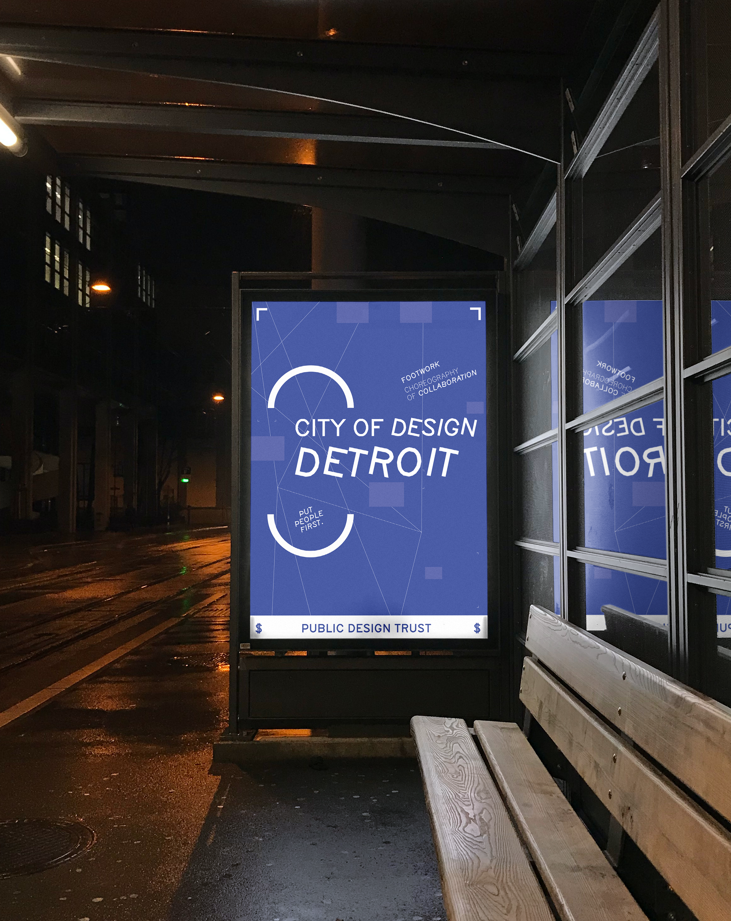 A bus stop shelter at night with a digital advertisement display promoting the City of Detroit's design initiatives, with a wooden bench nearby and wet street pavement reflecting light.
