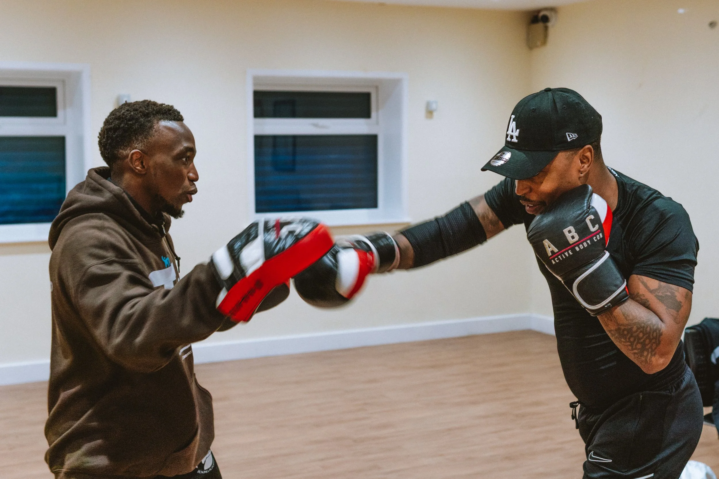 Two men training in boxing inside a room, with one man throwing a punch at the other, who is wearing boxing gloves.