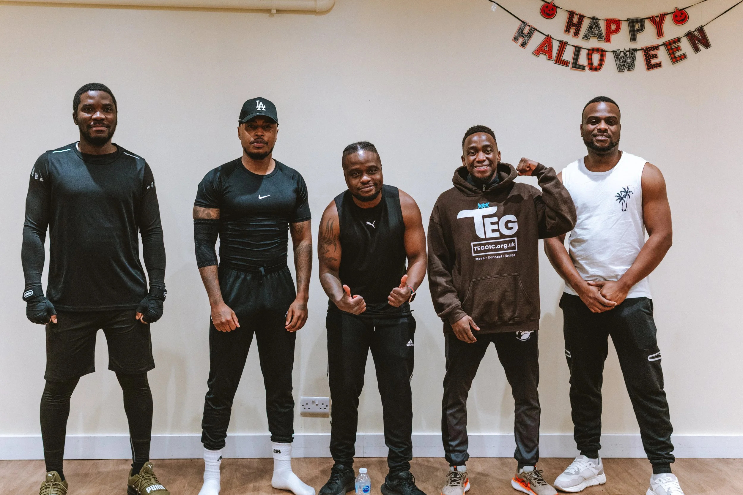 Five men standing in a room with a 'Happy Halloween' banner hanging on the wall behind them.